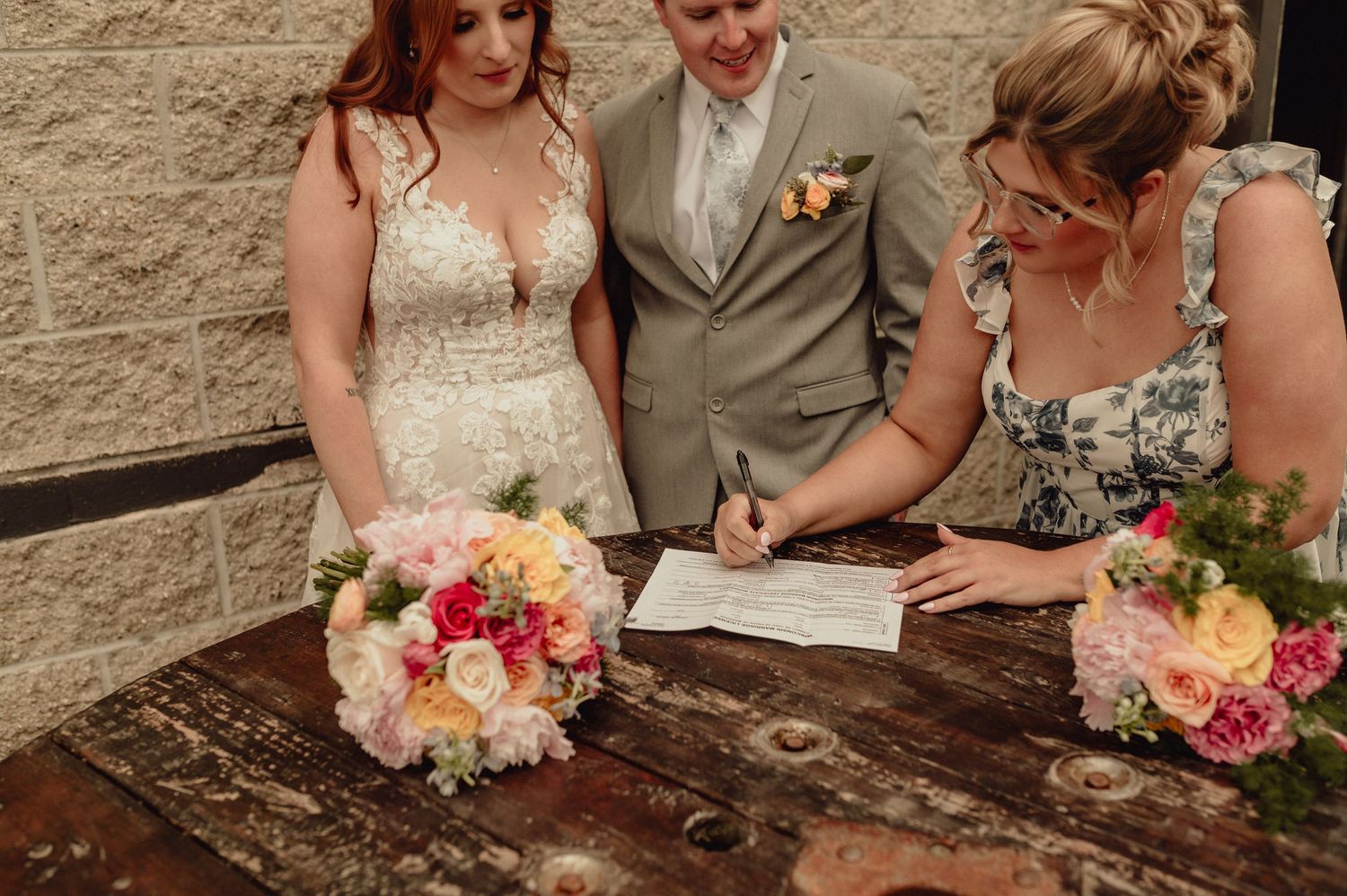 A collage of wedding photos showing floral bouquets, document signing, and formal attire against a stone wall backdrop.