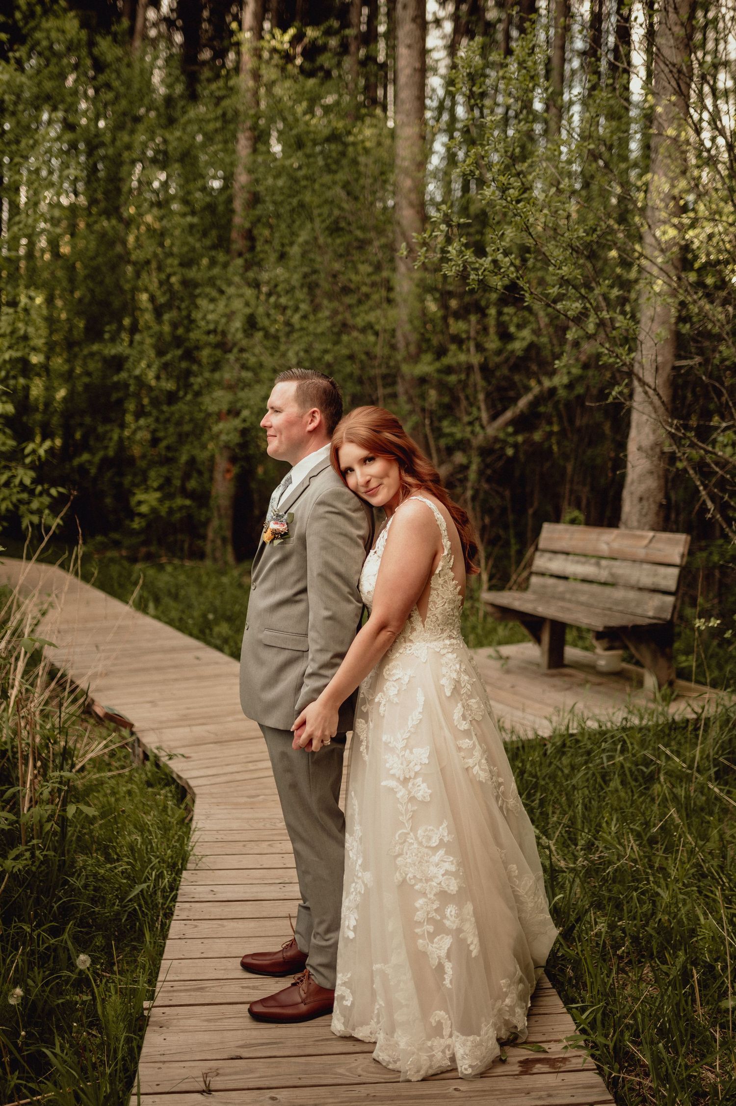 A couple shares a romantic moment on a wooden boardwalk surrounded by lush forest greenery.