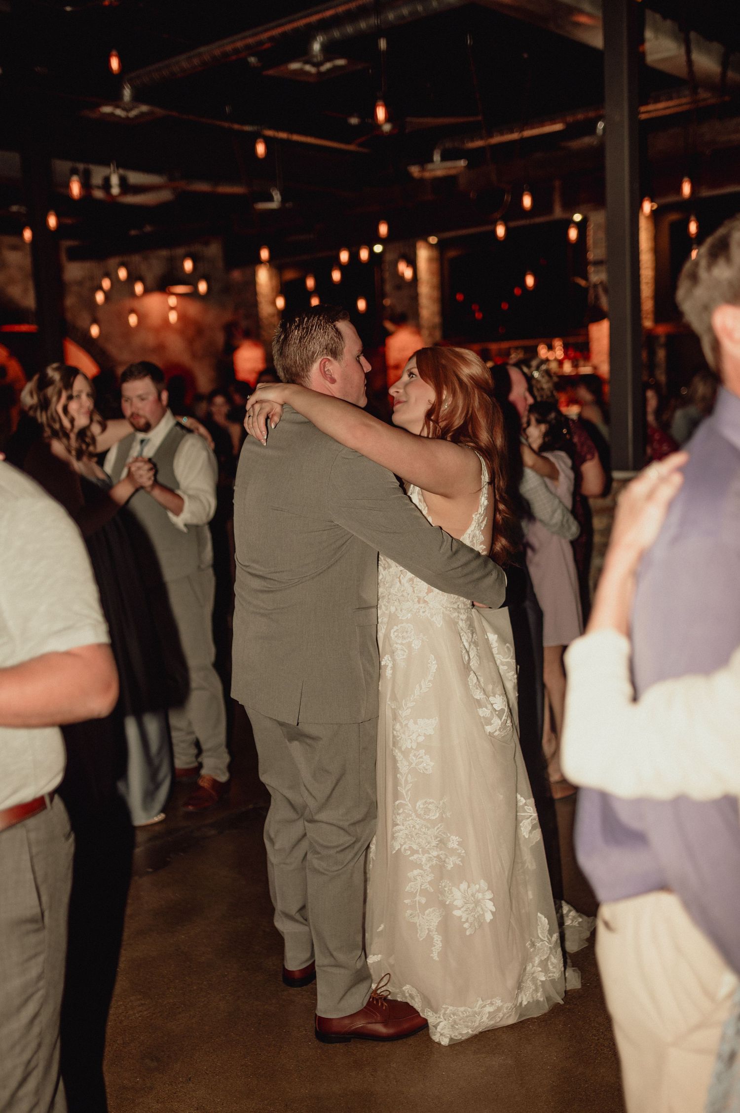 Couples slow dancing at a dimly lit wedding reception with warm ambient lighting and exposed ceiling beams.