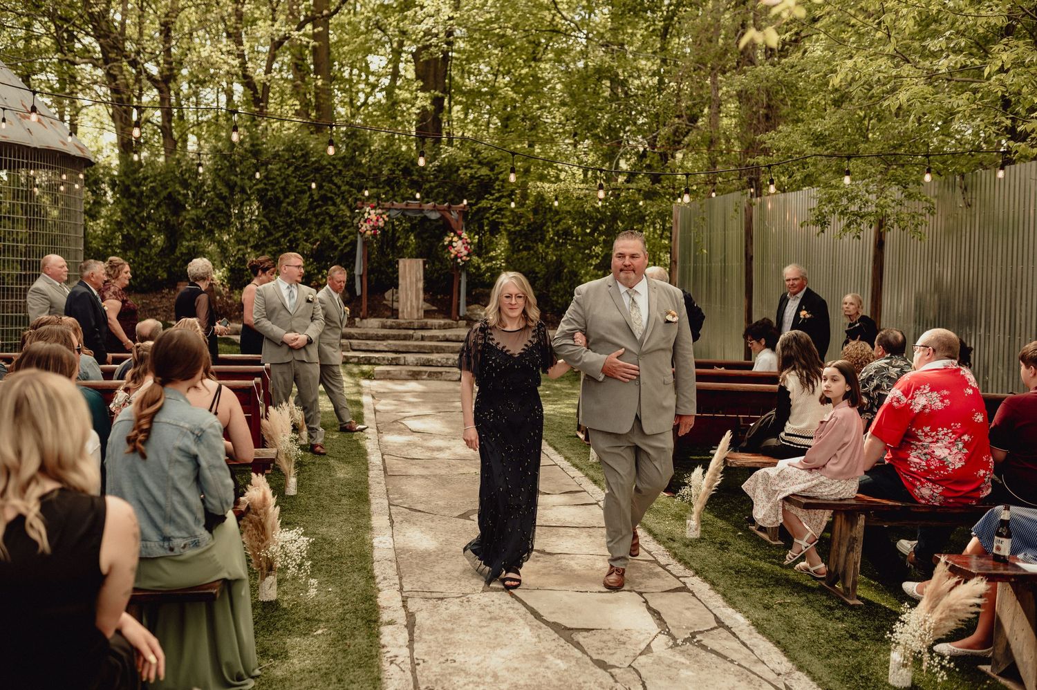 A group of wedding guests mingle and socialize in a lush outdoor garden setting during a summer celebration.
