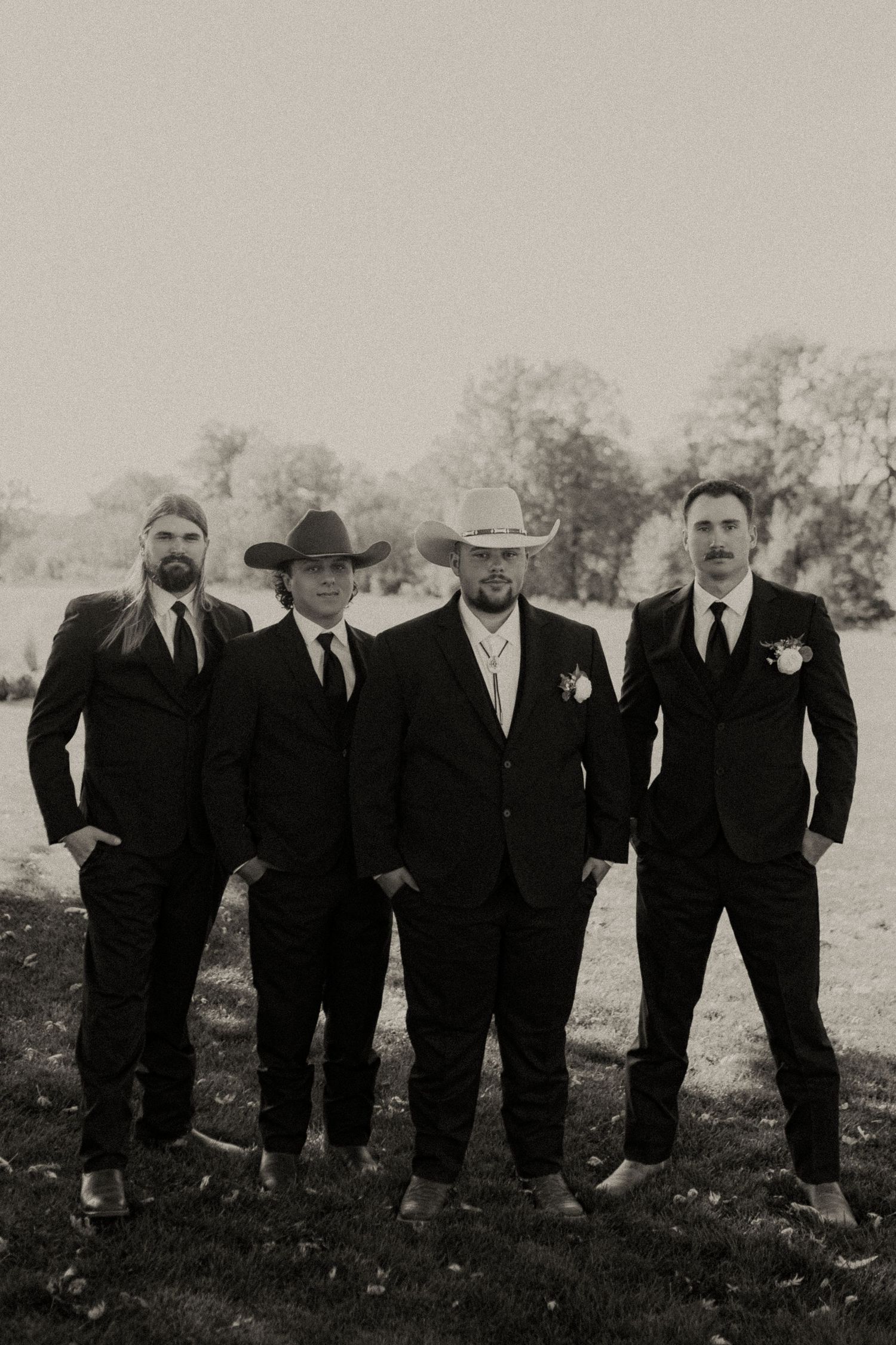 Groomsmen in black suits posing together outdoors in black and white photography.
