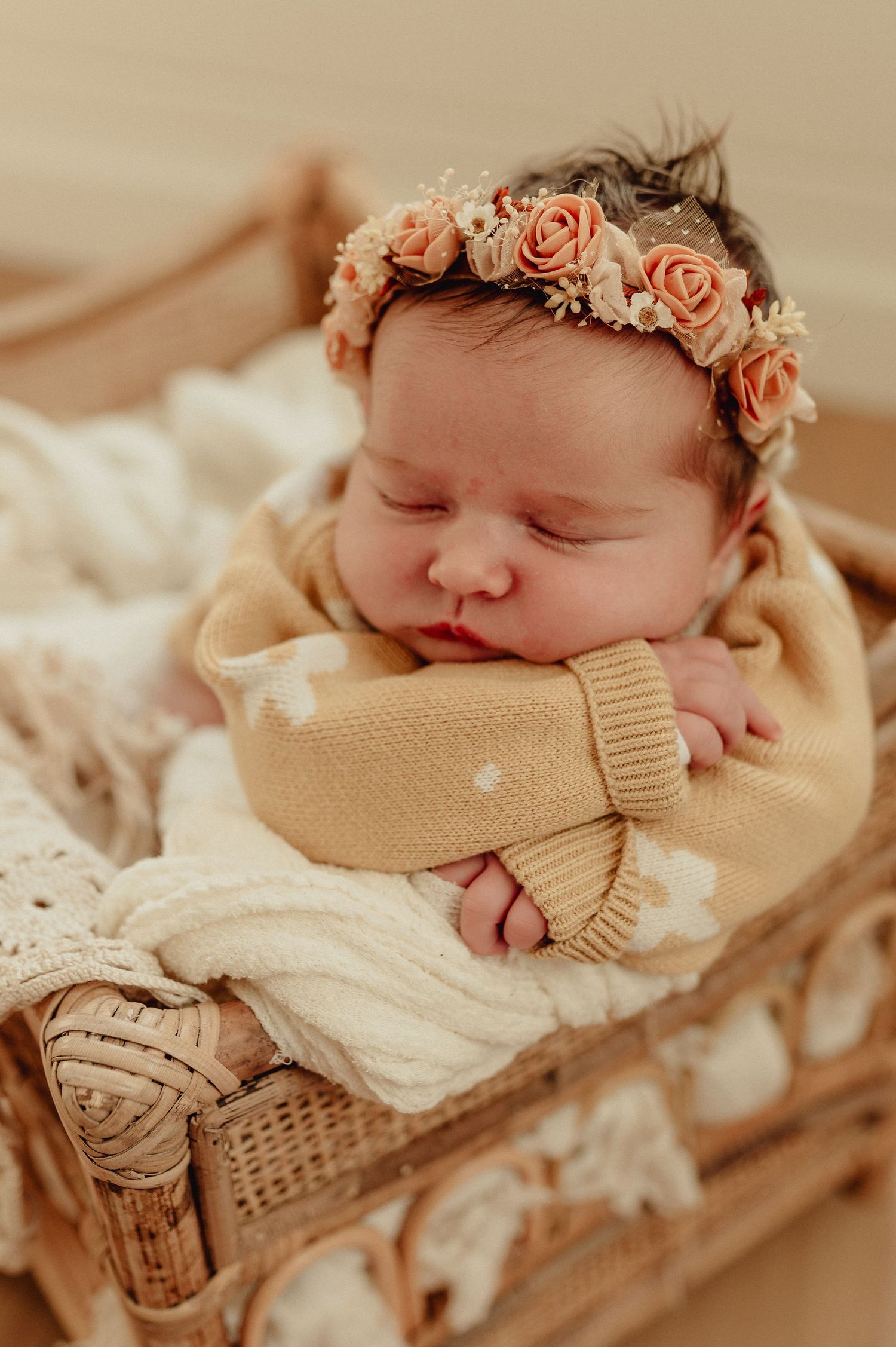 Peaceful sleeping newborn wearing floral crown and wrapped in cream colored blanket.