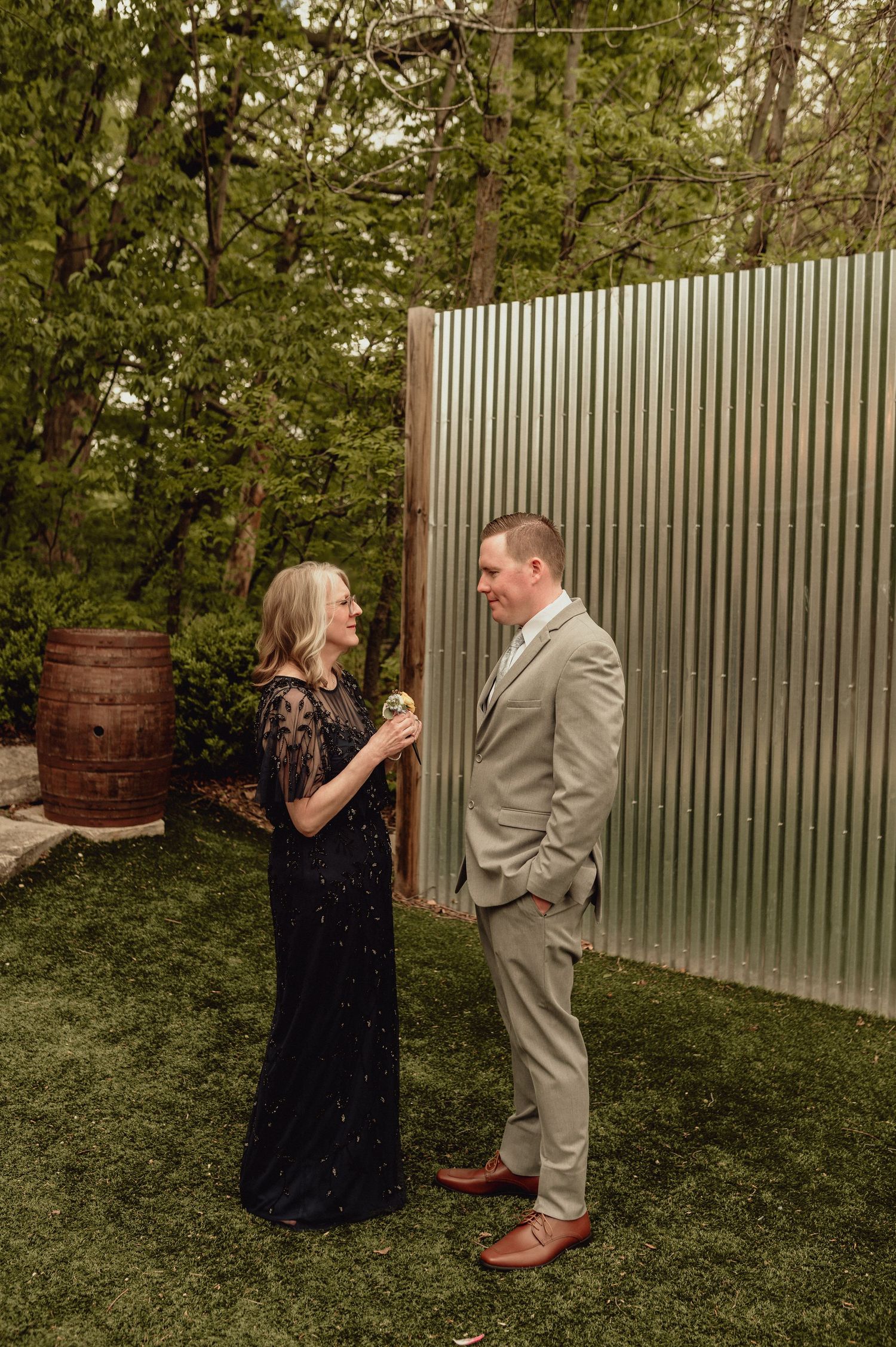 A couple shares a joyful moment outdoors, dancing and laughing together in a garden setting with a metal fence backdrop.