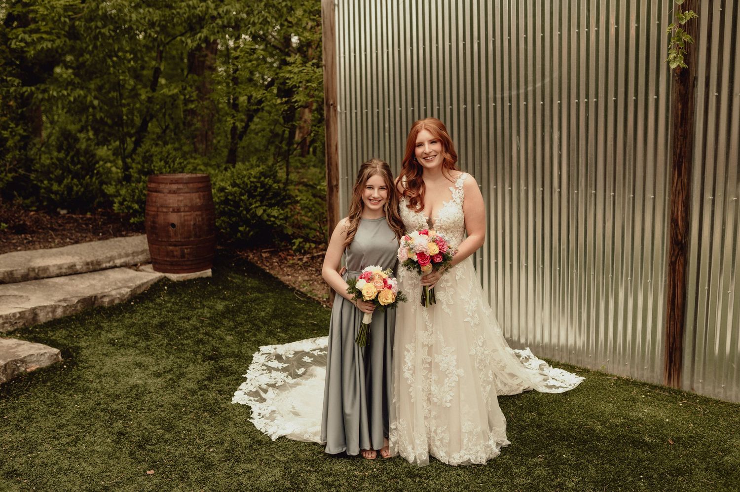 Wedding party members pose in front of a rustic metal wall with lush greenery in the background.