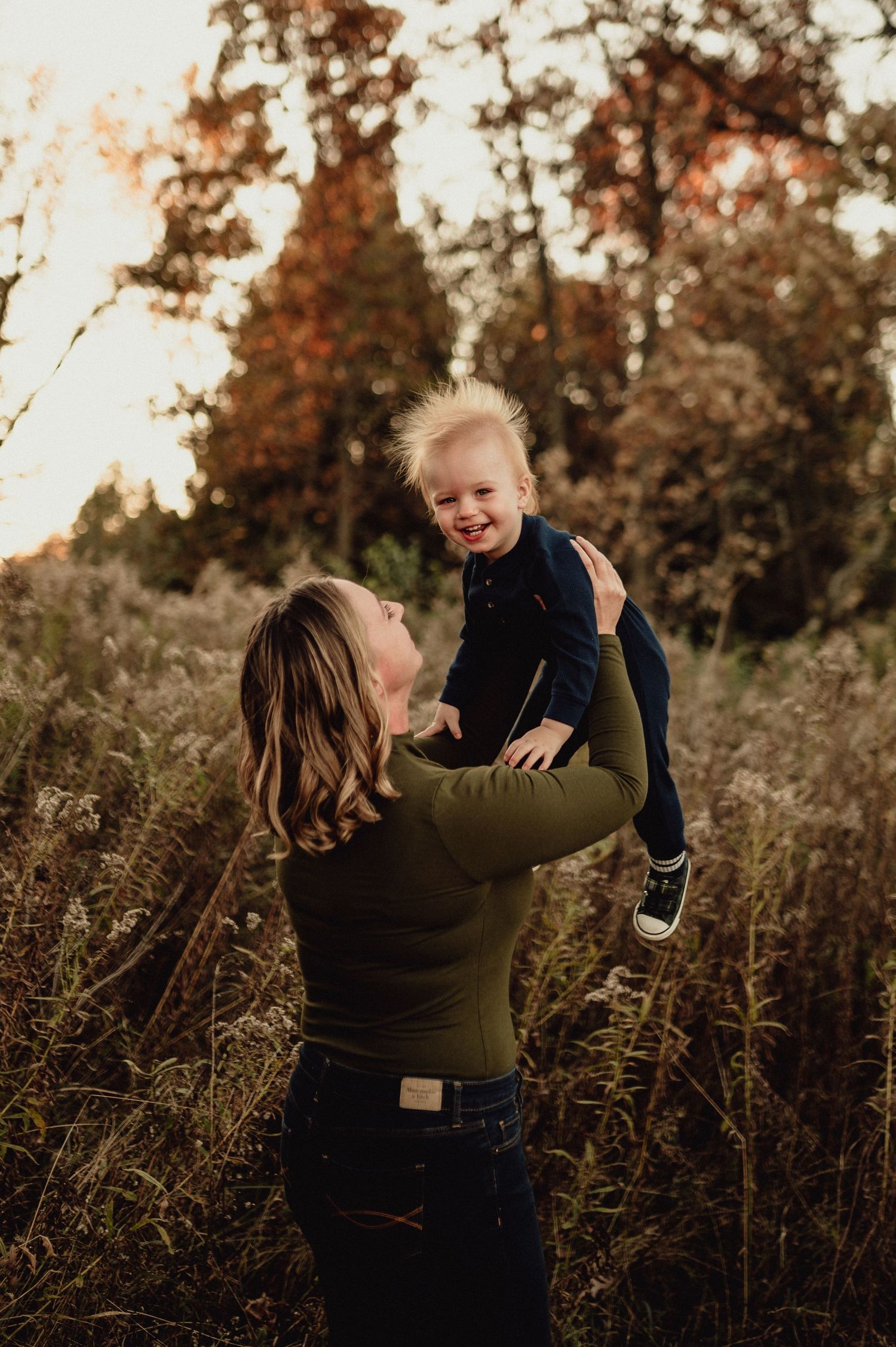 Parent lifting child playfully during golden hour in autumn field.