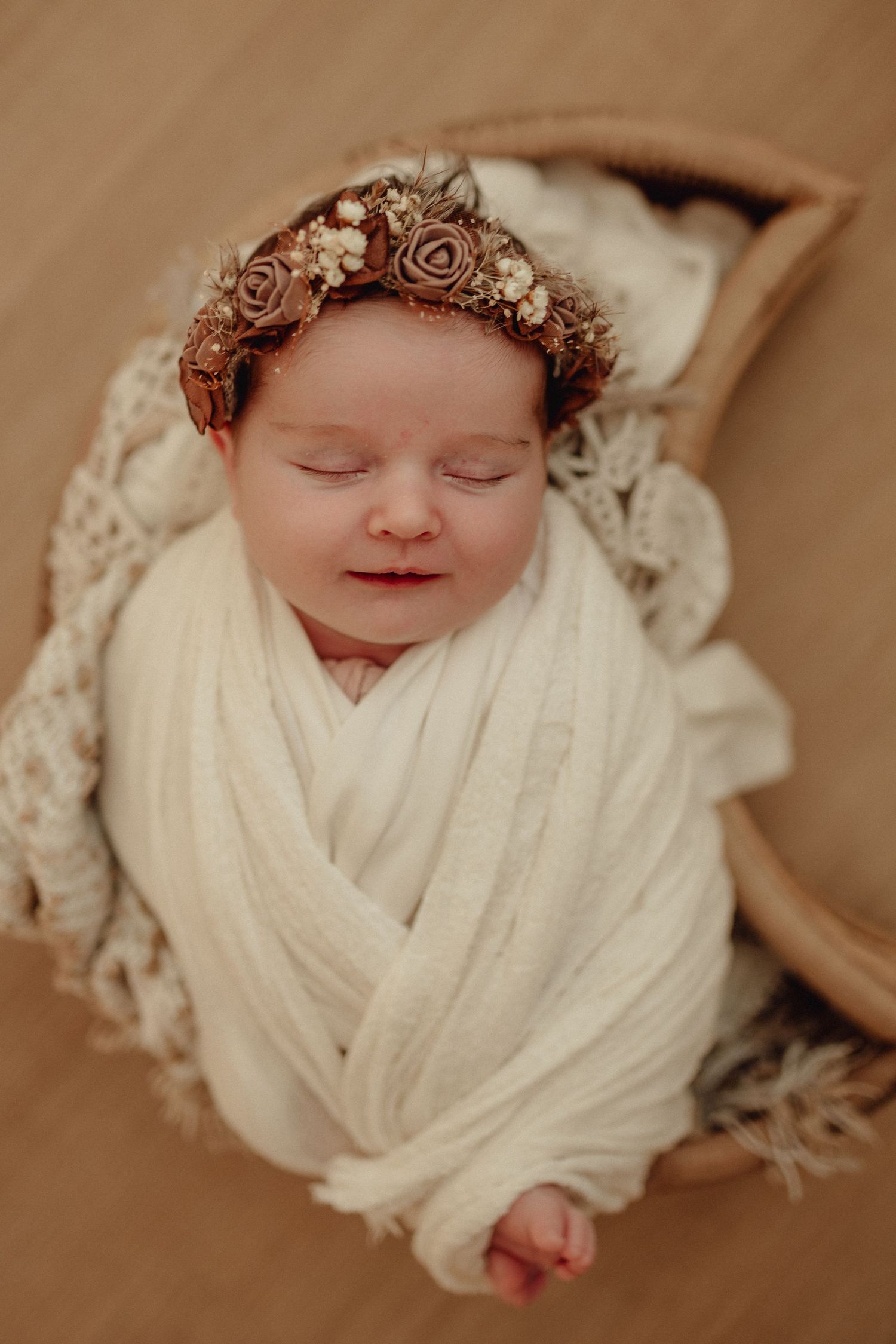 Overhead view of sleeping newborn wrapped in white with delicate floral headpiece.
