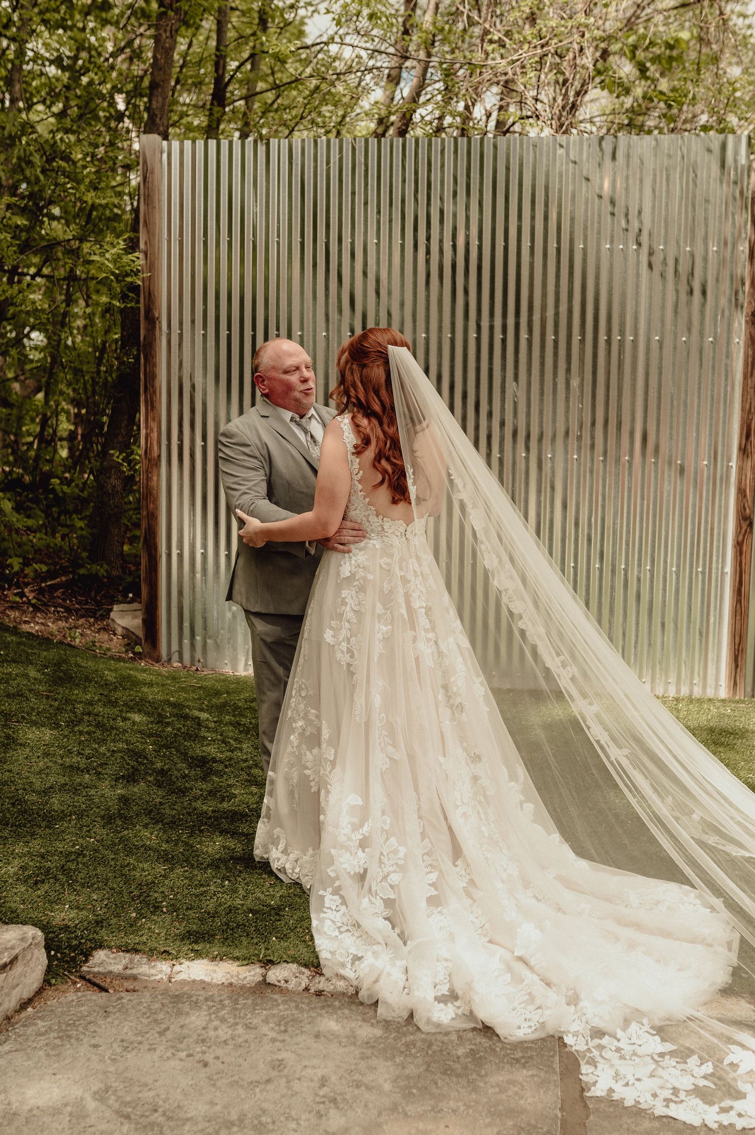 A romantic wedding couple shares an intimate moment against a white wall backdrop with lush greenery in the background.