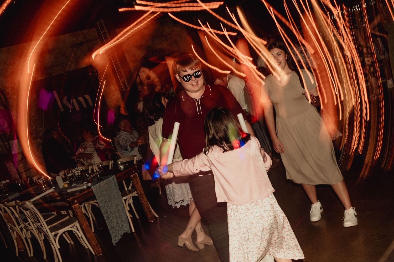 Wedding reception guests dance under warm orange lighting on a dark dance floor.