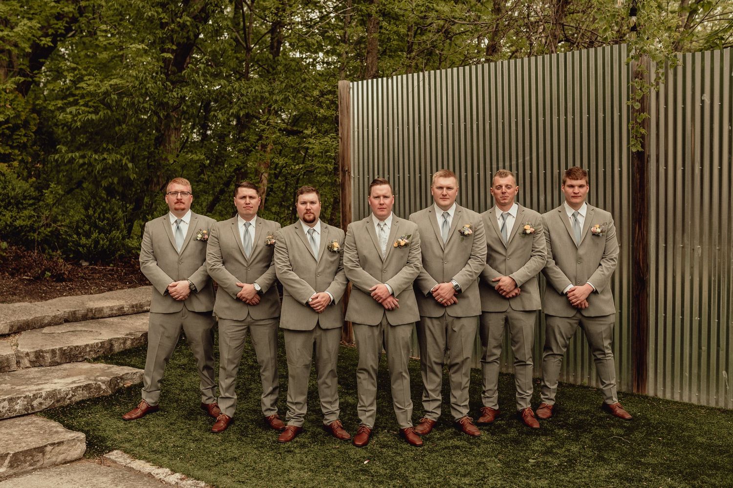 A group in gray suits and red socks pose on stone steps in an outdoor garden setting.