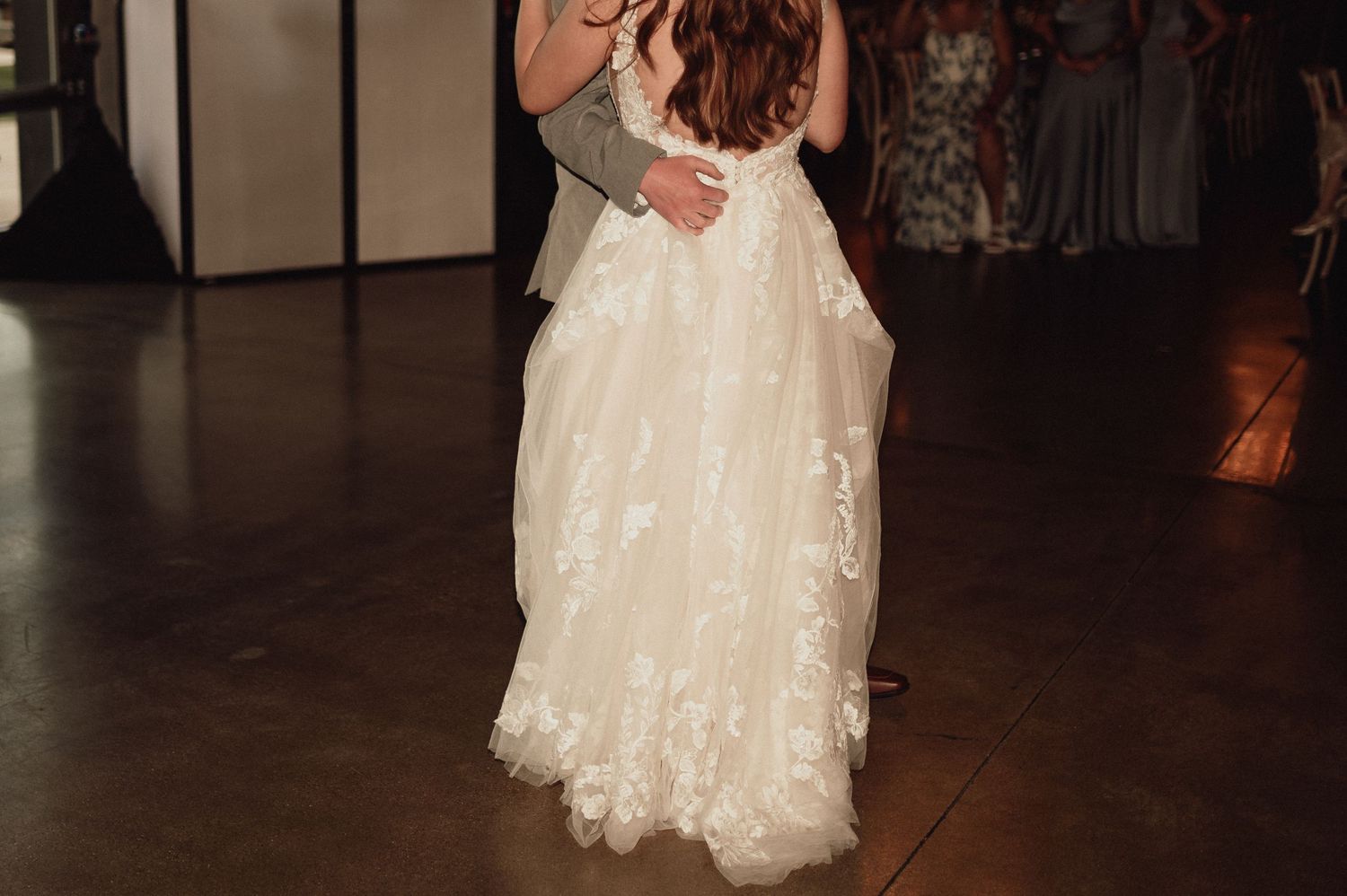 Elegant white lace wedding gown with flowing tulle skirt shown on dark hardwood dance floor.