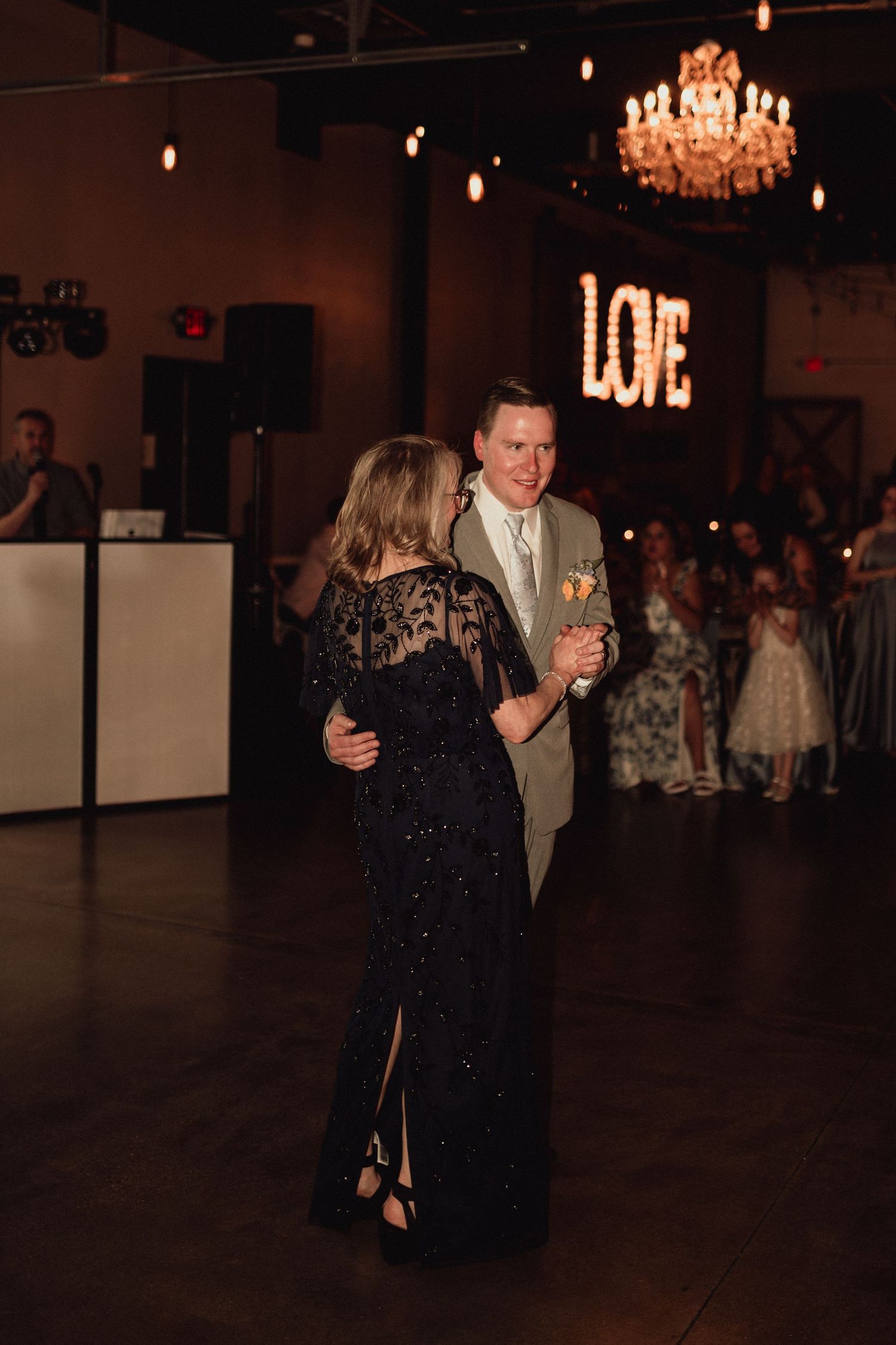 Couples dance together in a dimly lit ballroom with chandeliers and romantic lighting creating an elegant atmosphere.
