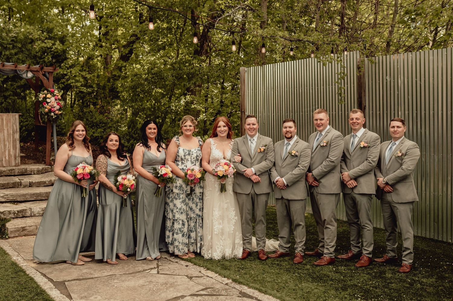 Wedding party in gray and white attire poses together outdoors for formal group photos.