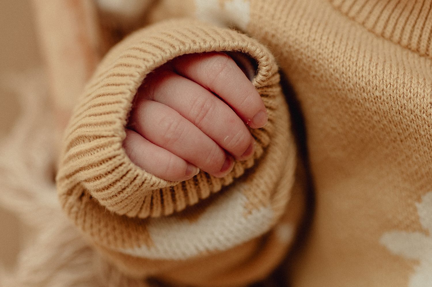 Close-up detail of tiny baby feet in soft beige knitted booties.