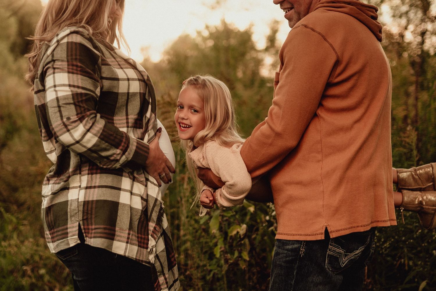 Couple embracing during maternity shoot wearing plaid and rust colored sweater.