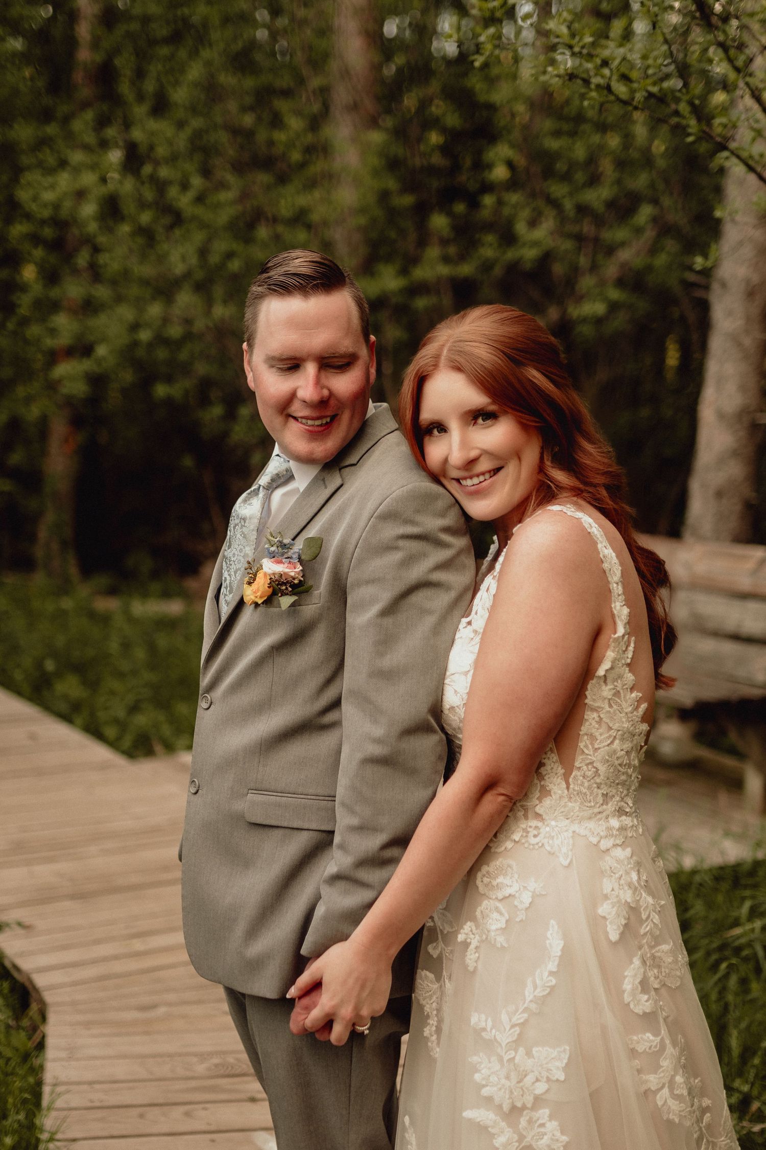 A couple in wedding attire shares joyful moments on a wooden boardwalk surrounded by lush greenery.