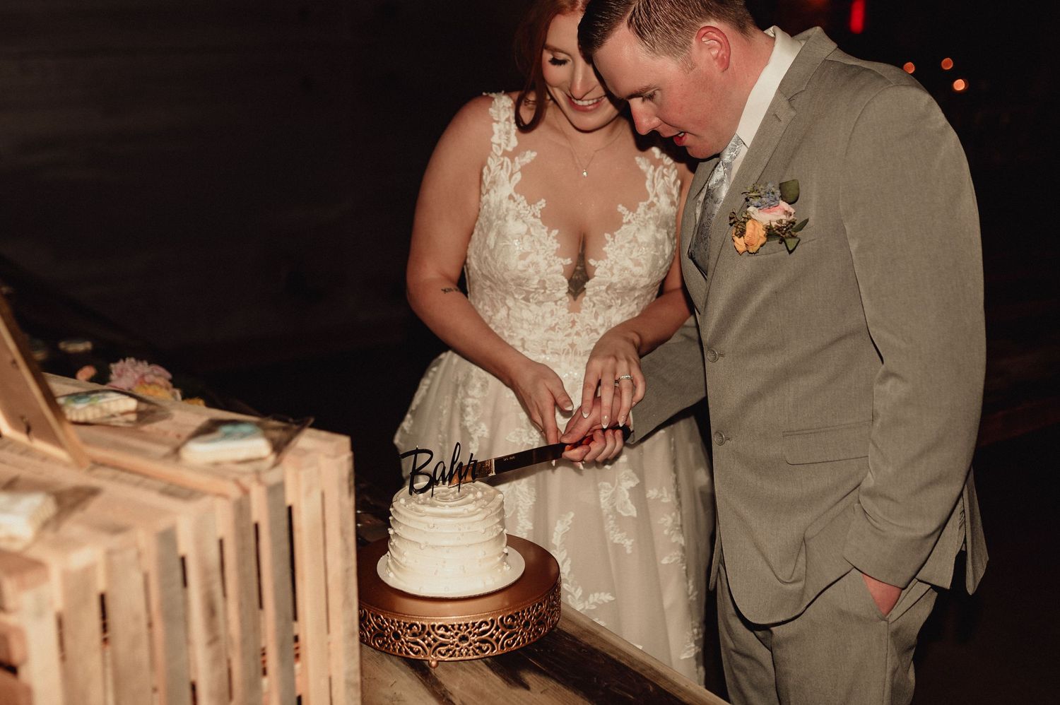 A couple in wedding attire cuts their rustic three-tiered wedding cake adorned with floral decorations.