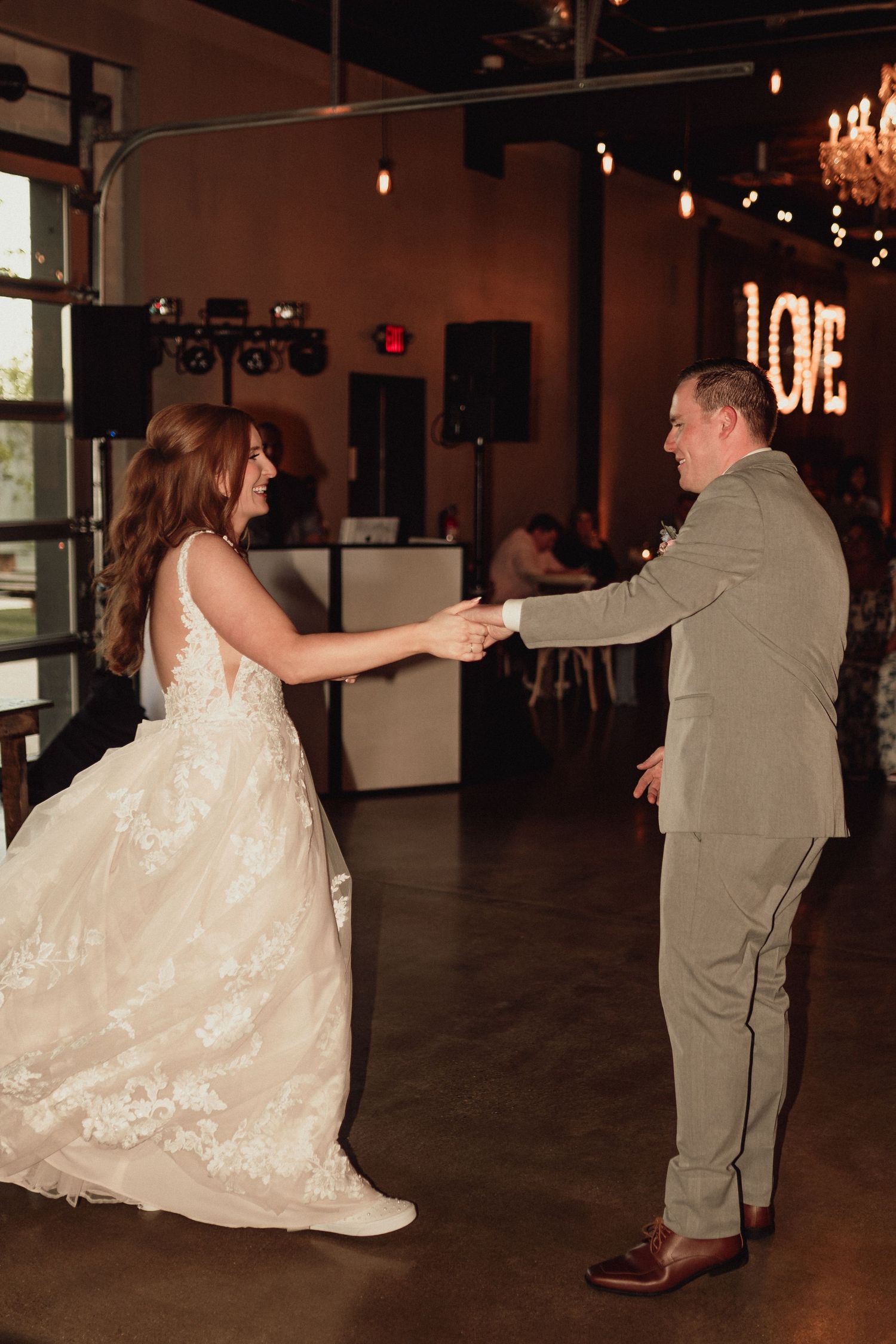 A couple shares a dance together at a wedding reception in a dimly lit venue with a chandelier in the background.