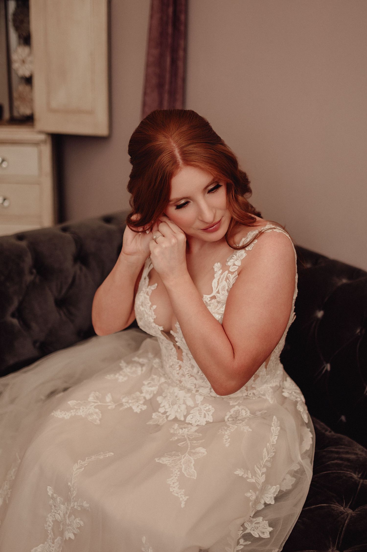 A bride in a white lace wedding dress poses gracefully on a dark velvet couch in a series of romantic portraits.
