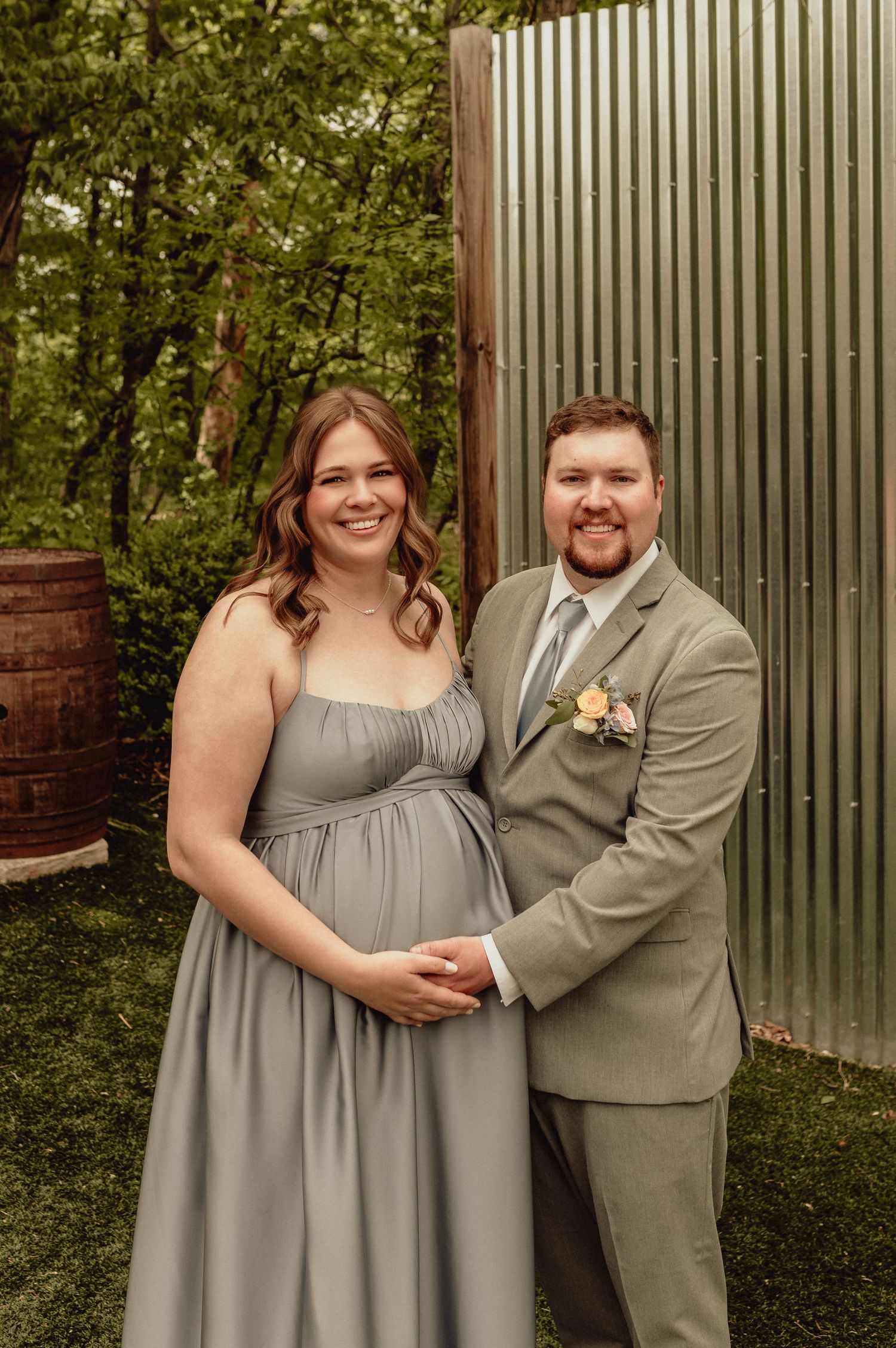 A couple in gray wedding attire poses together against a corrugated metal wall in an outdoor garden setting.