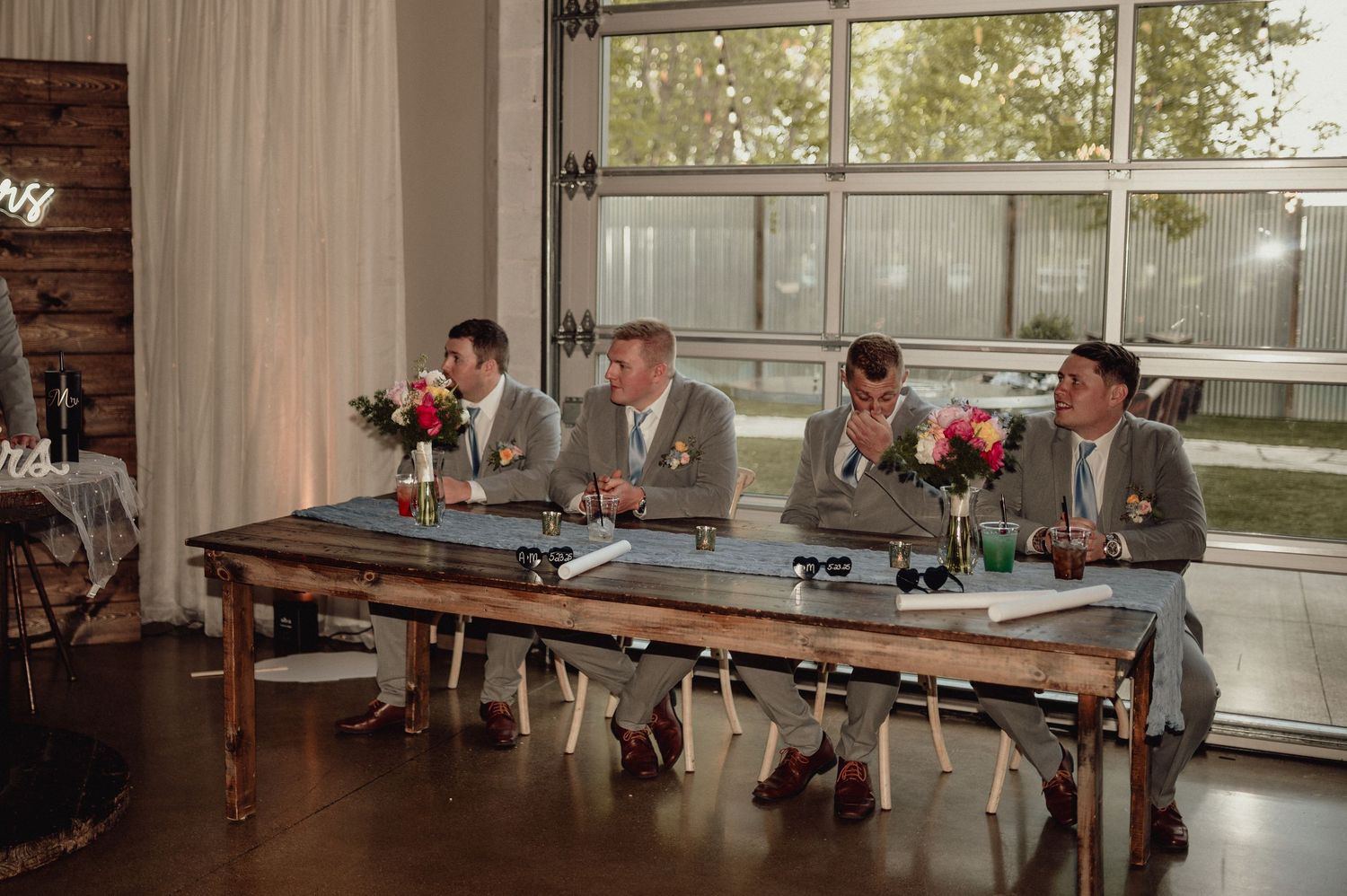 A group gathers around a long wooden table in a rustic cabin setting with natural light streaming through windows.