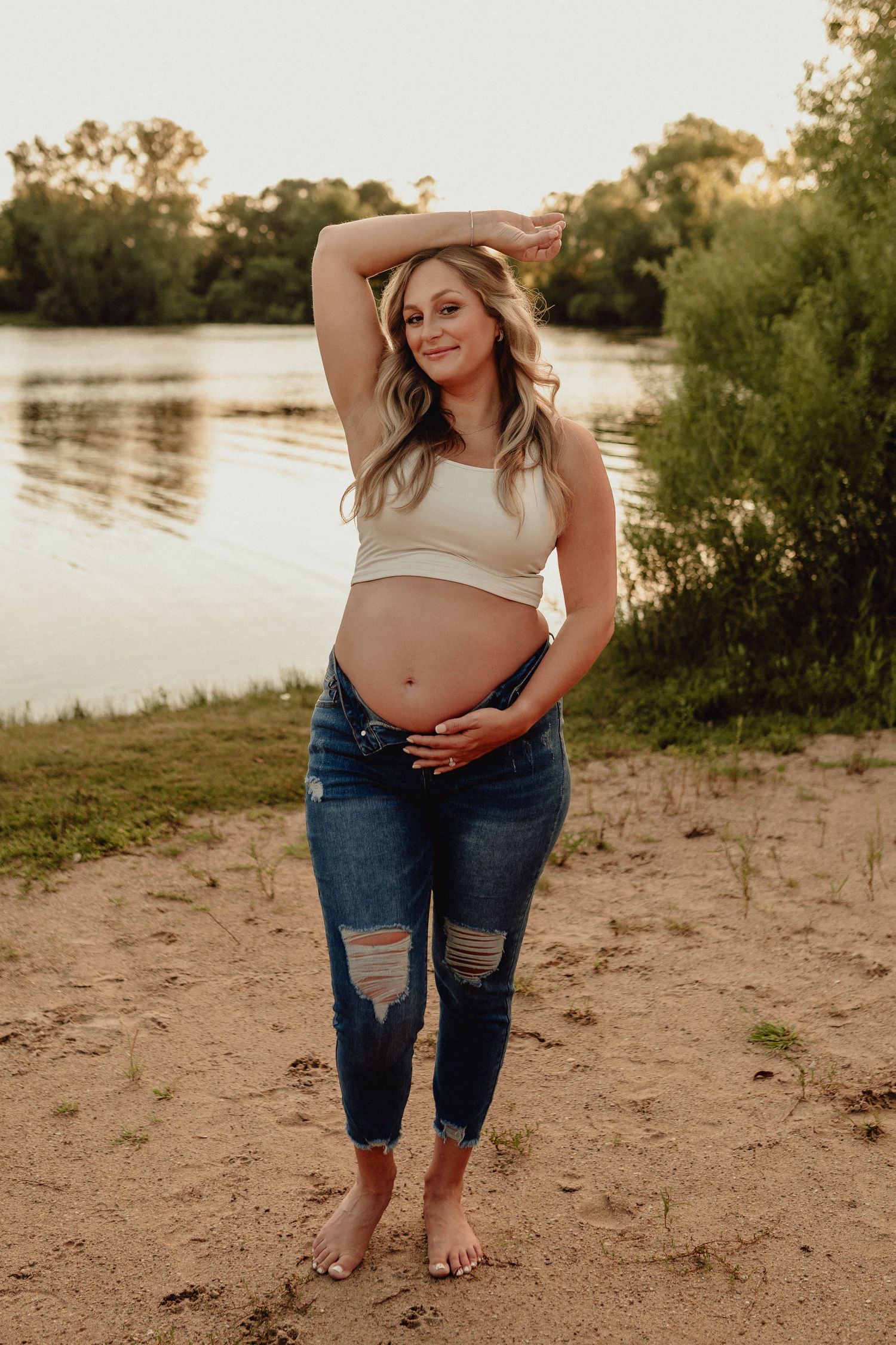 Casual maternity photos on beach showing pregnant belly and ripped jeans.