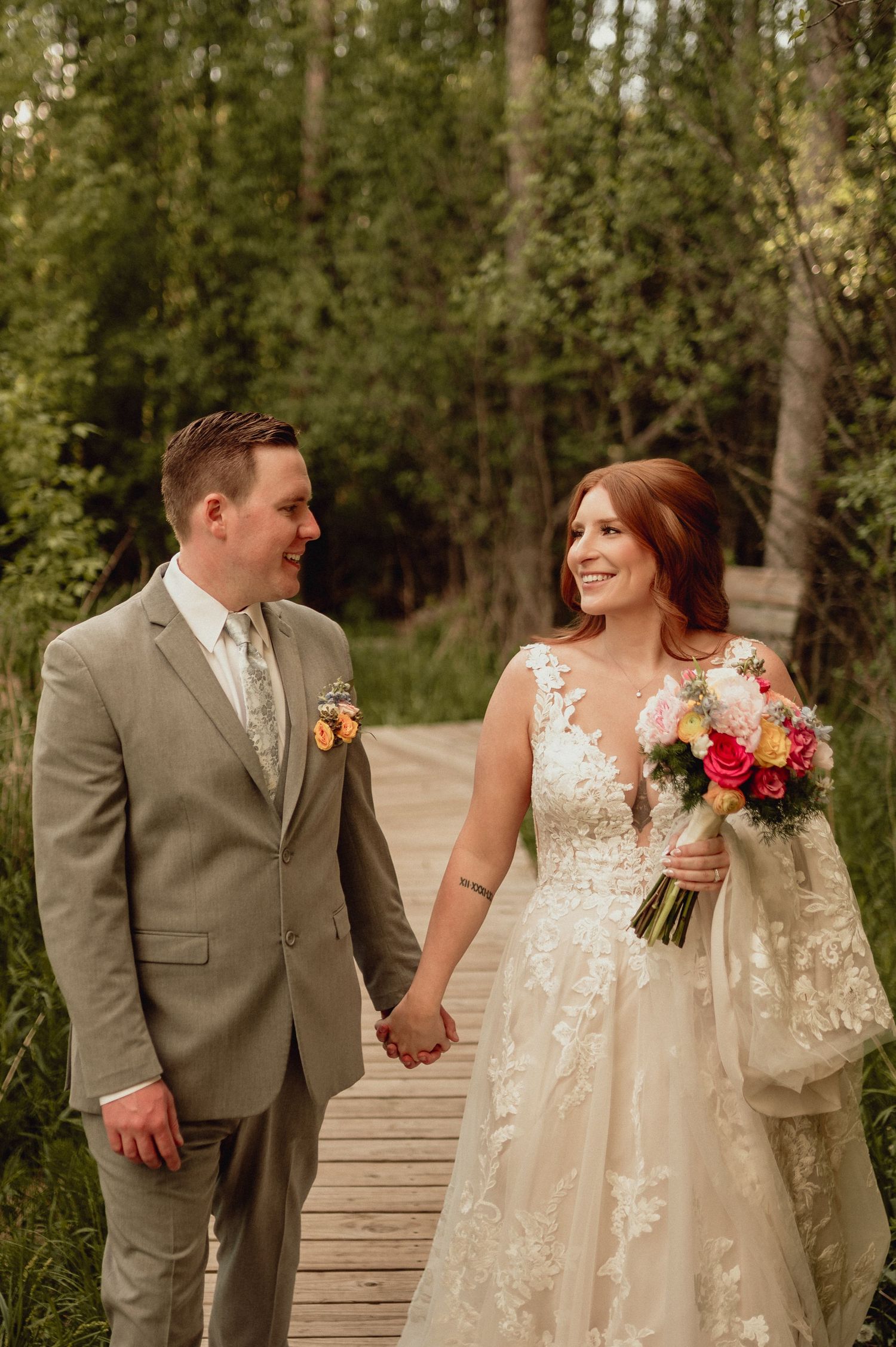A couple shares joyful moments on a wooden boardwalk surrounded by lush greenery during their wedding photoshoot.
