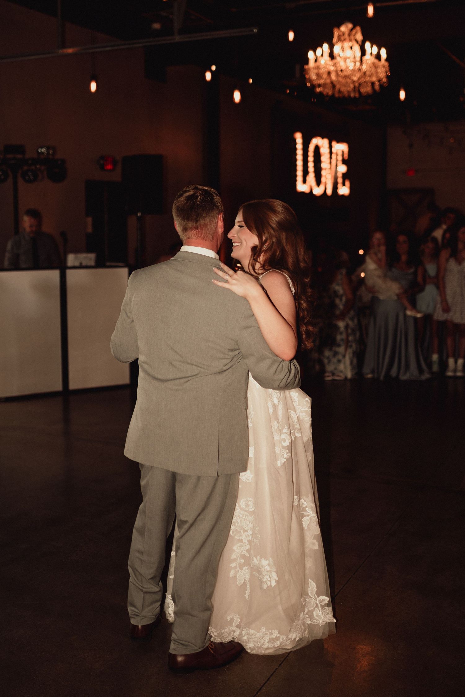 A bride and groom share an intimate slow dance together under a chandelier at their wedding reception.