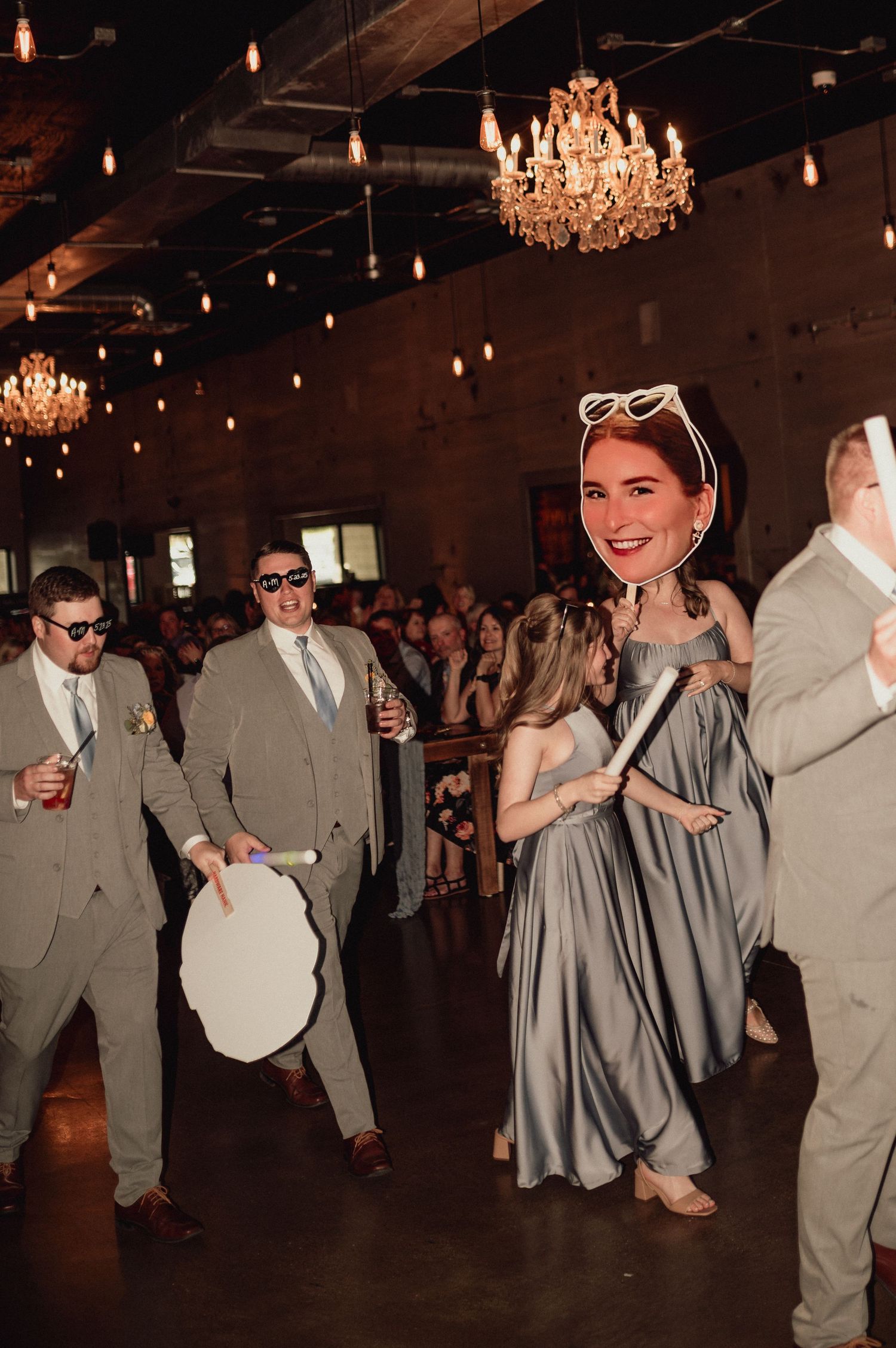 Wedding guests dance and celebrate on the dance floor under a crystal chandelier at an elegant reception venue.