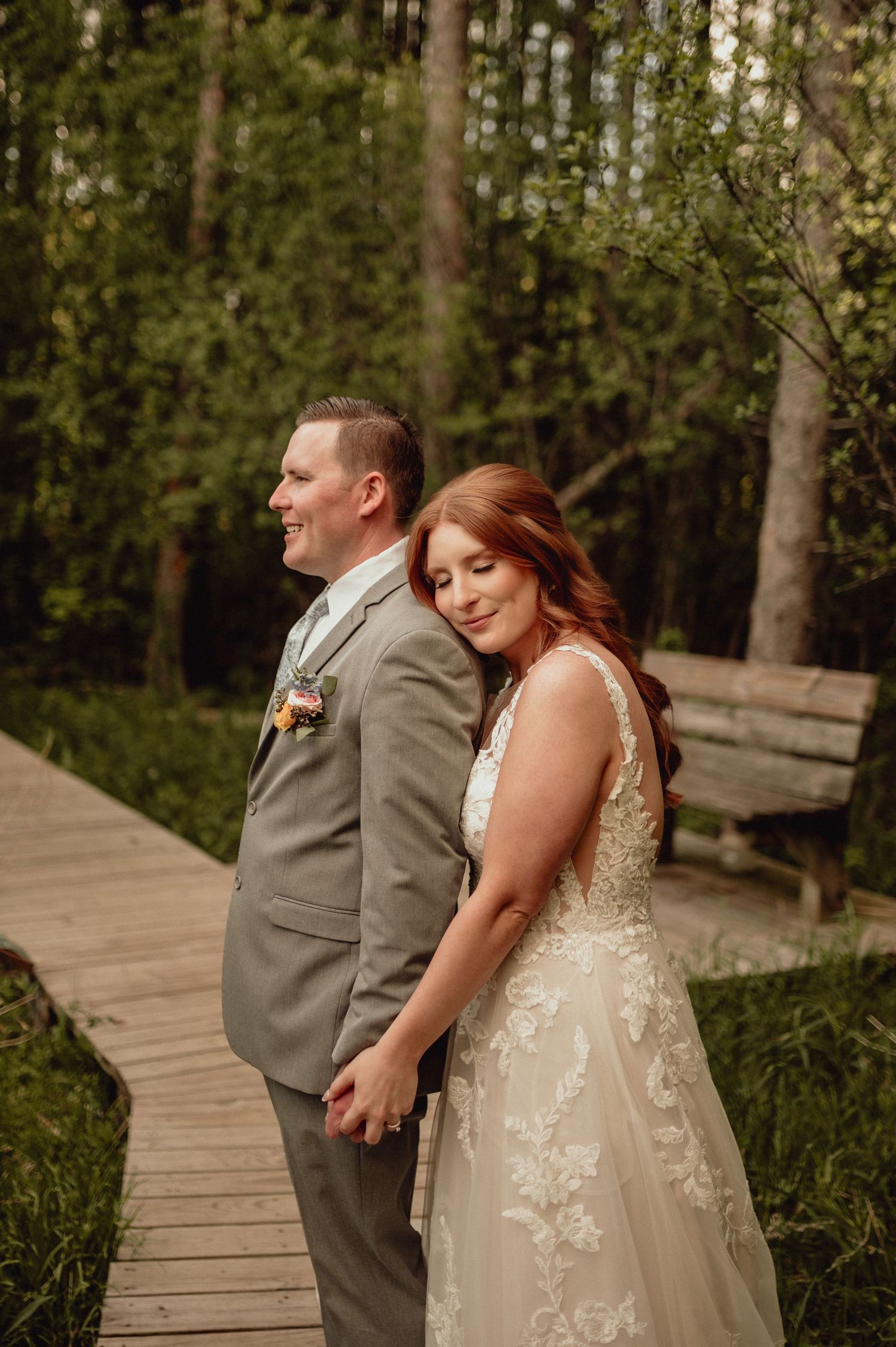 A couple in wedding attire share intimate moments on a wooden boardwalk surrounded by lush greenery.