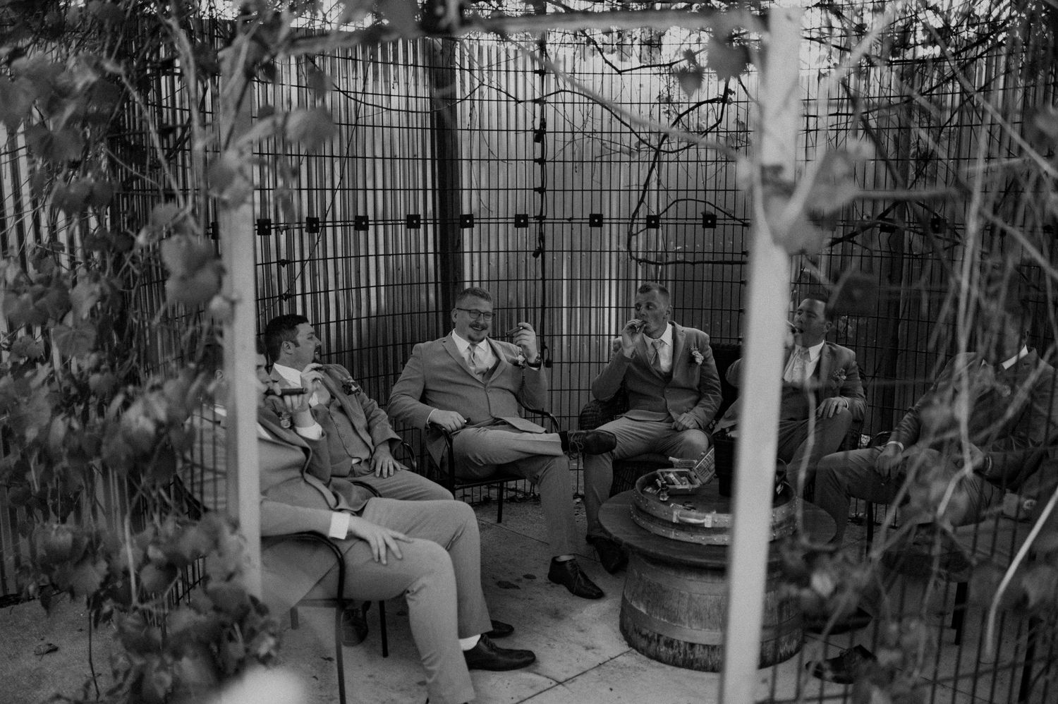 A black and white photograph shows a backyard garden with metal fencing, potted plants, and patio furniture.