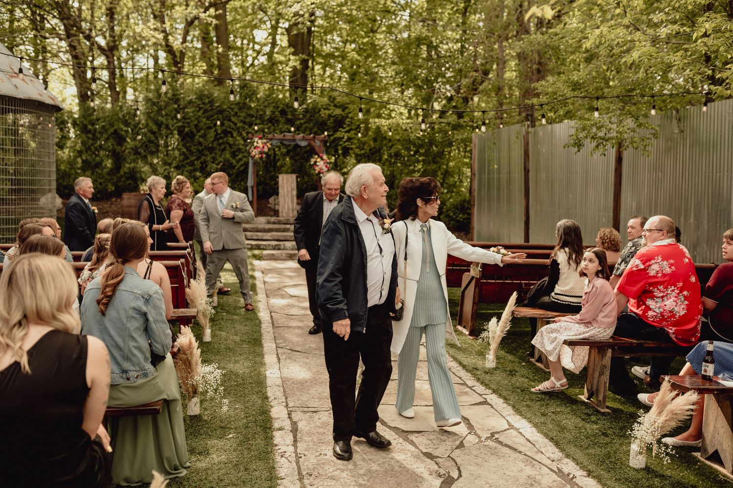 Wedding guests gather outdoors in a garden setting for a casual celebration on a sunny afternoon.