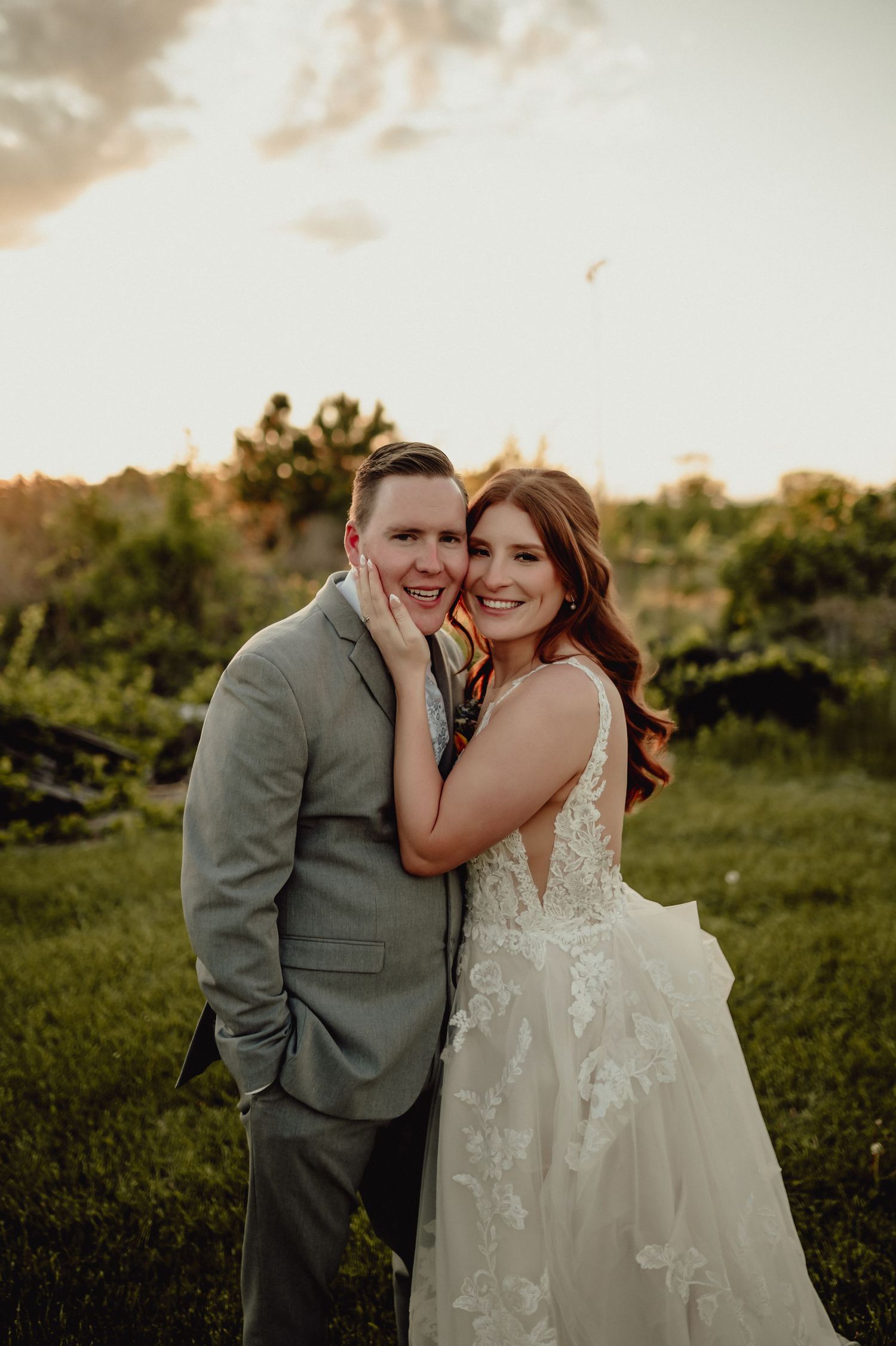A romantic wedding couple shares joyful laughter together in a lush outdoor setting during golden hour.