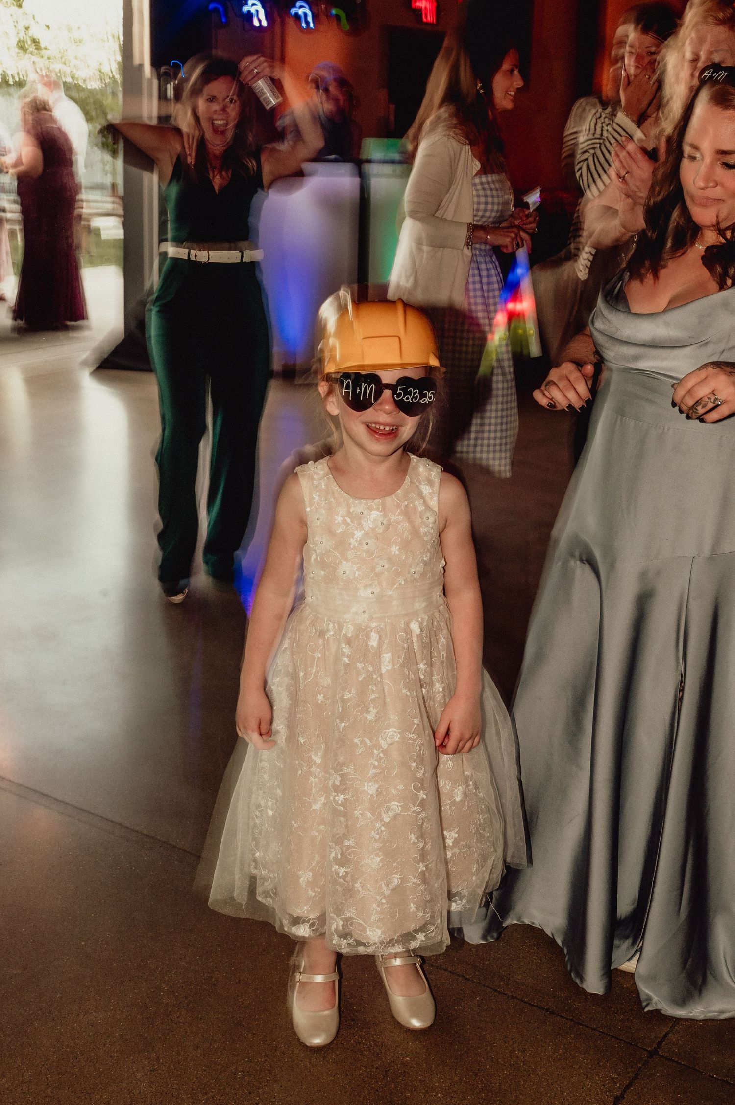 A young party guest in a sparkly white dress and sunglasses poses on the dance floor at a formal celebration.