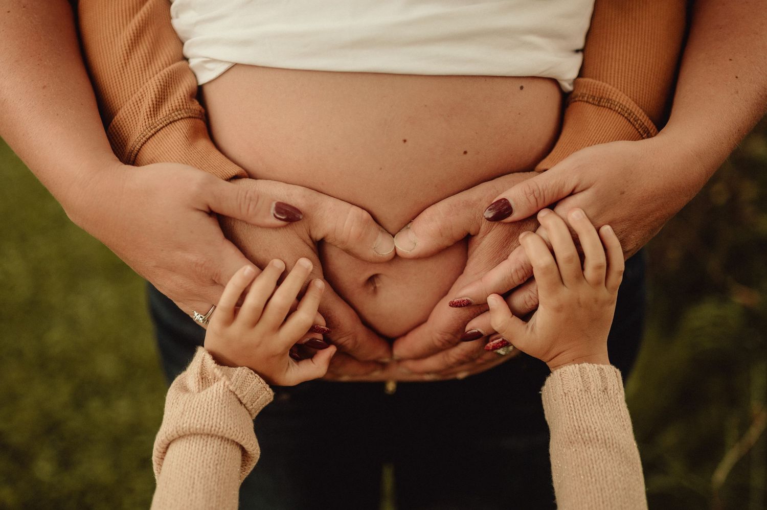 Close up details of hands cradling pregnant belly in outdoor setting.