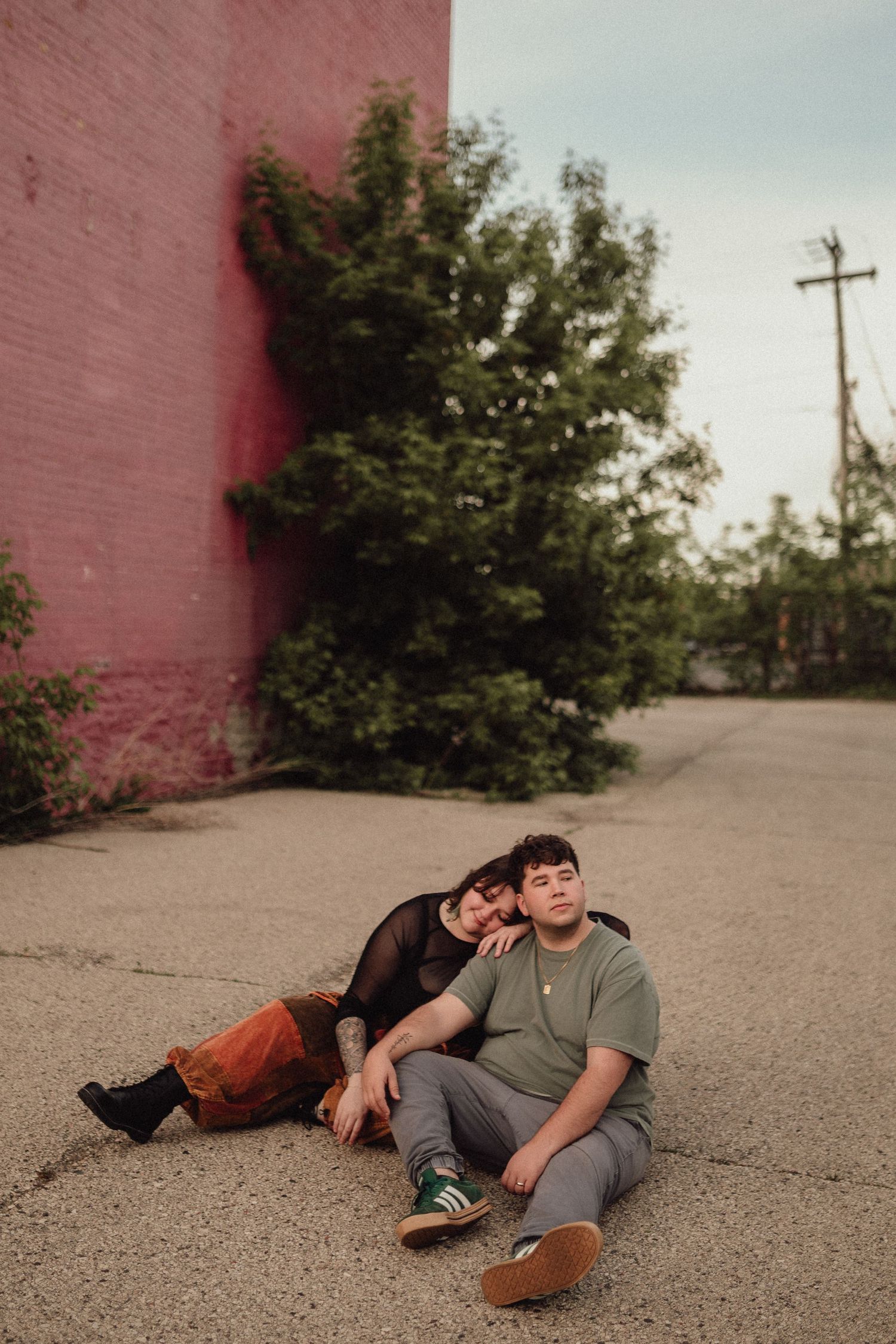 Artistic engagement photo session against a pink brick wall outdoors.
