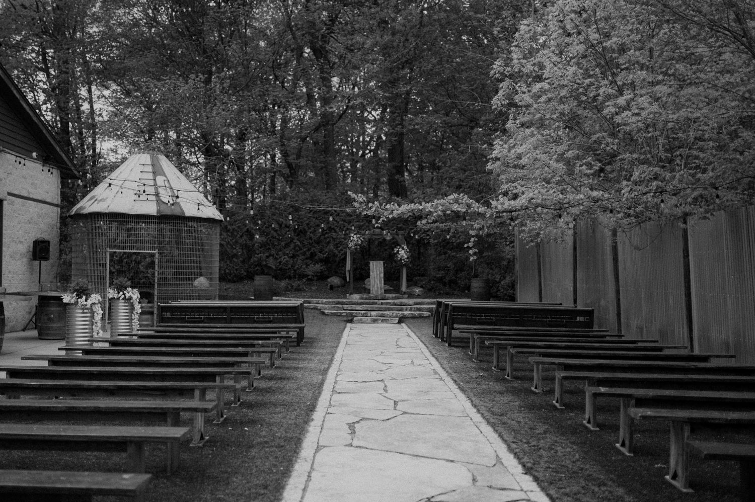 Black and white photo of wooden benches arranged in rows outdoors at a rustic church or camp meeting ground.