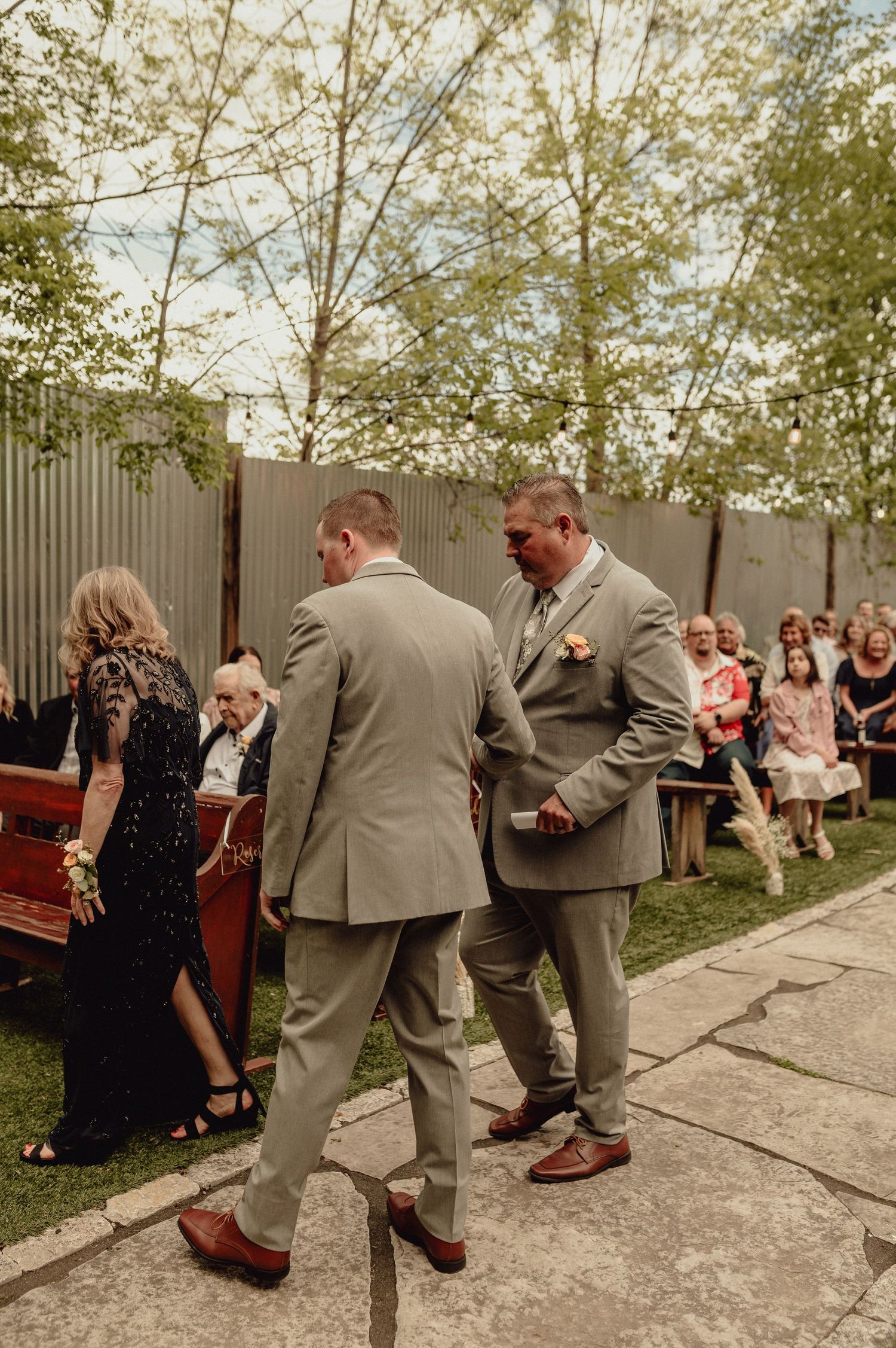 Wedding party members in gray suits perform a playful dance line on an outdoor patio during a celebration.