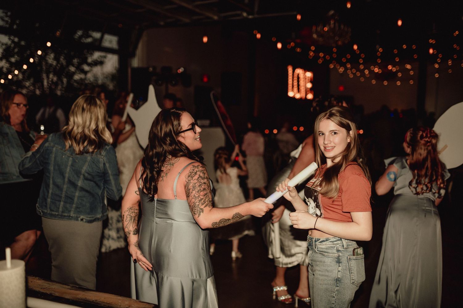 People dancing and socializing at a dimly lit party venue with string lights overhead.