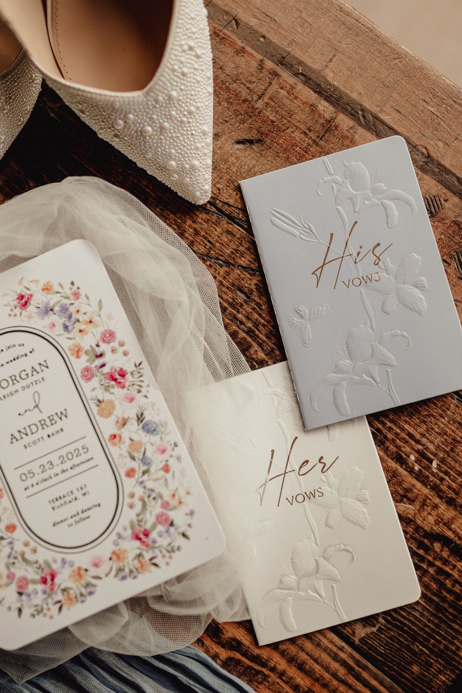 Wedding invitation suite featuring delicate floral designs, embossed details, and elegant typography on white paper against wood background.