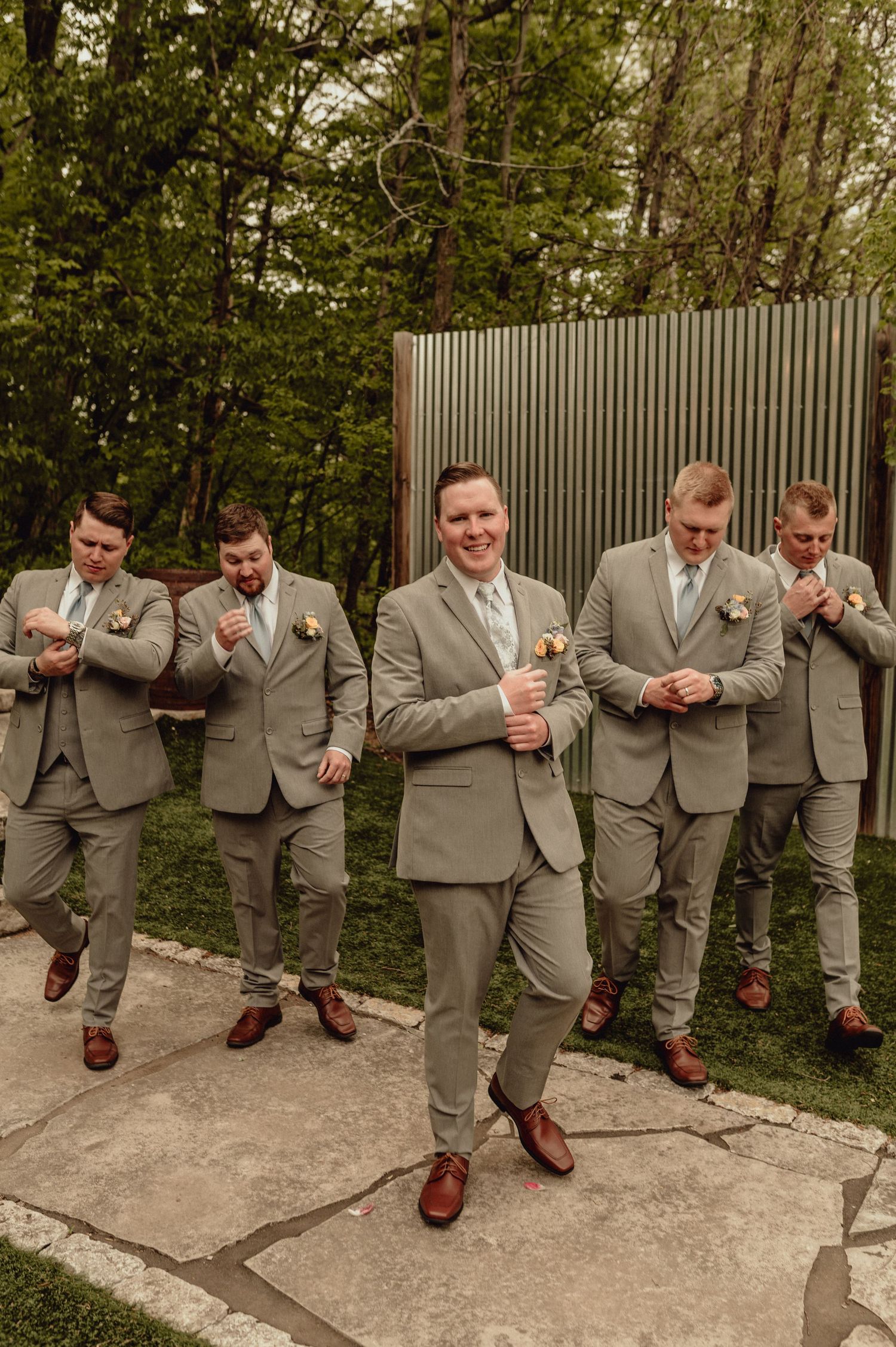 Groomsmen in matching gray suits show off their brown leather dress shoes in a playful outdoor photo series.