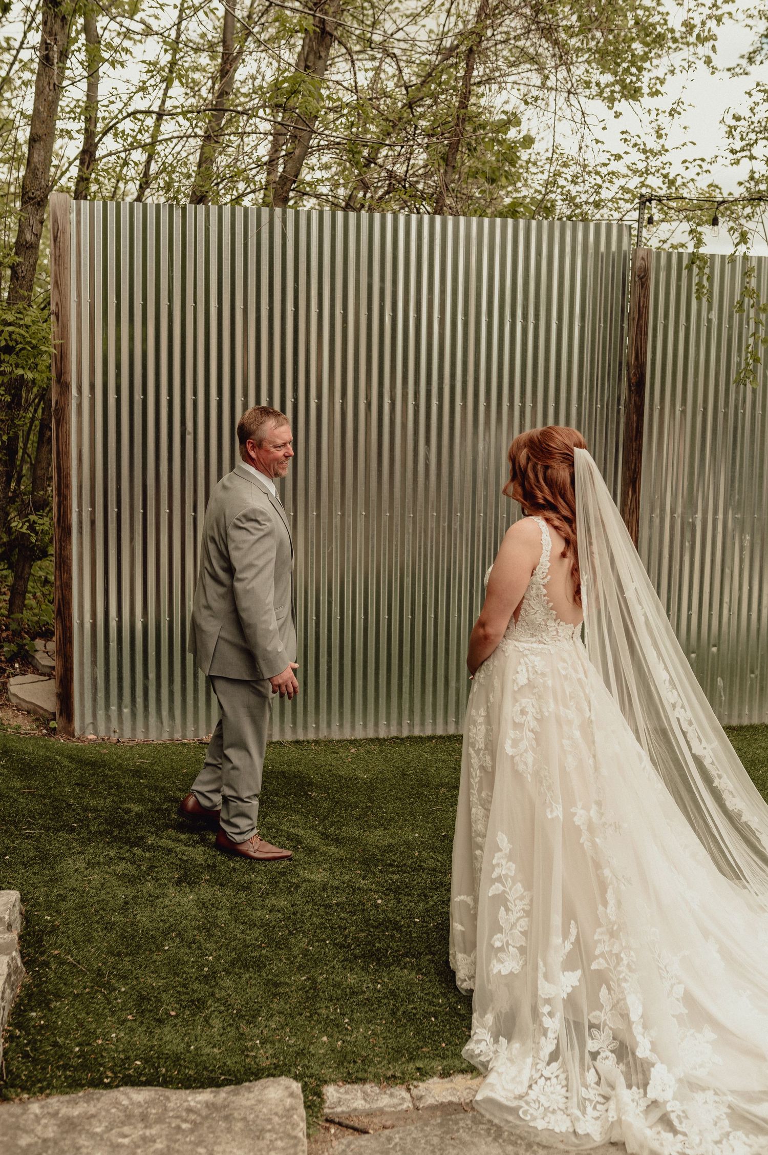 Emotional first look sequence between bride and groom in outdoor garden setting with lace wedding dress and grey suit.
