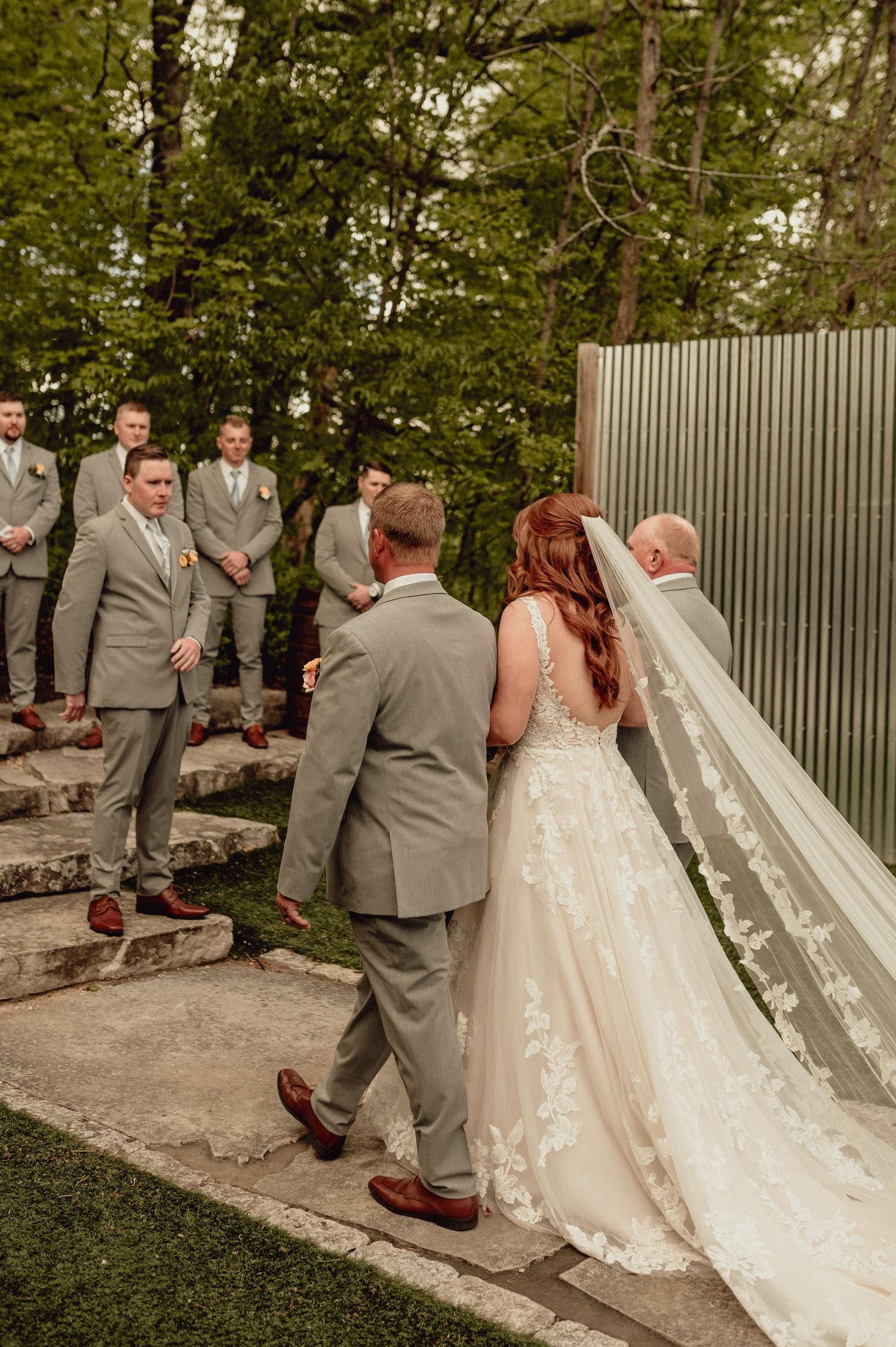 A first look moment between a bride in a flowing white dress and groom in grey suit on outdoor stone steps.