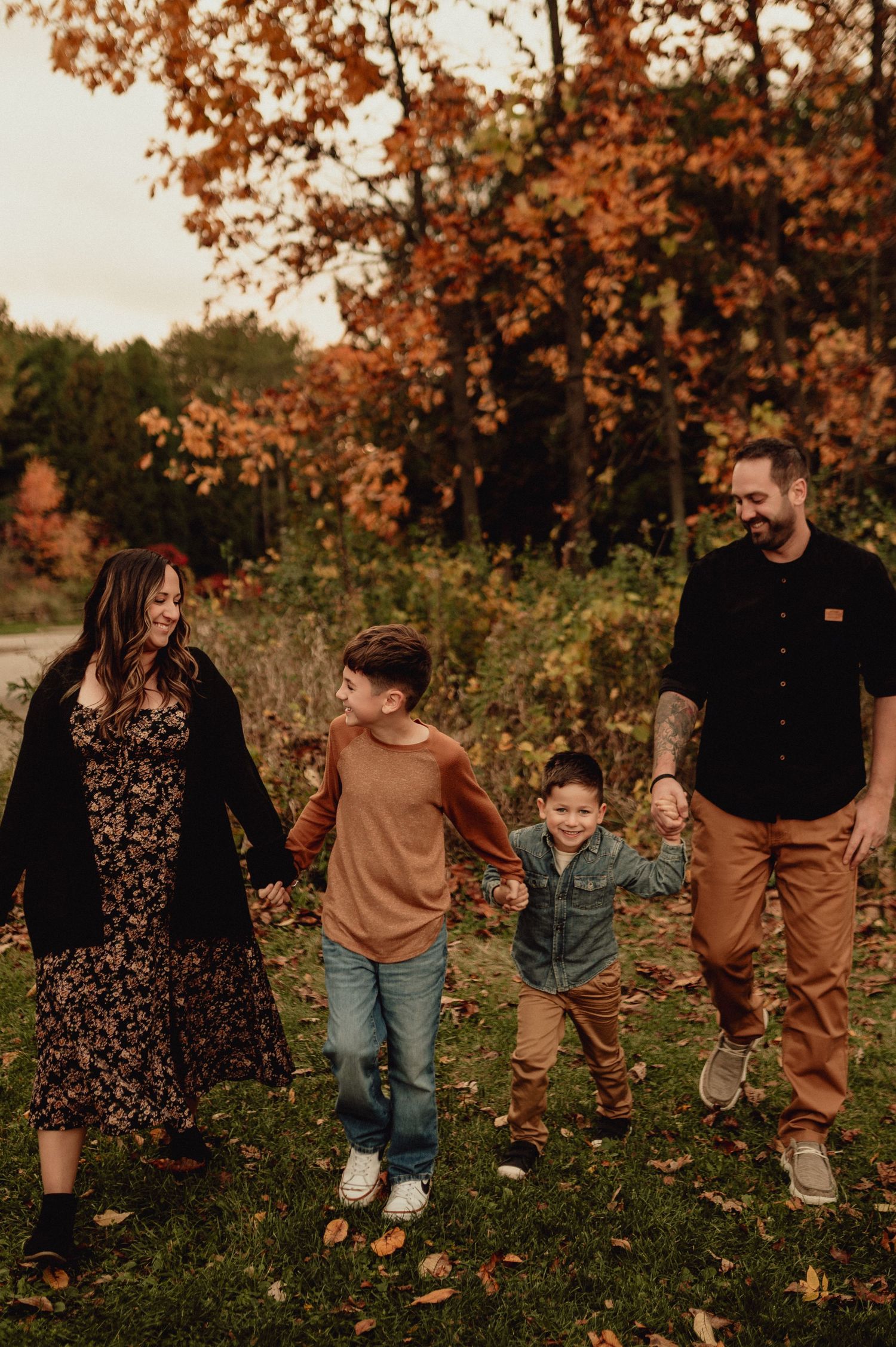 A family poses together in autumn foliage wearing coordinated brown and black outfits during golden hour.