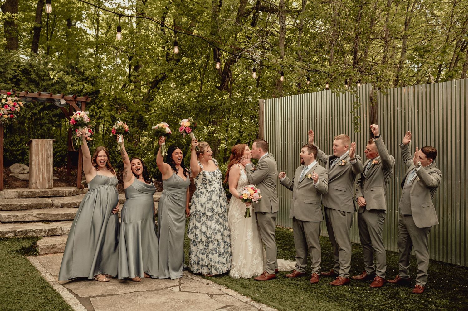 Wedding party stands in line outdoors wearing gray and white attire while making expressive gestures.