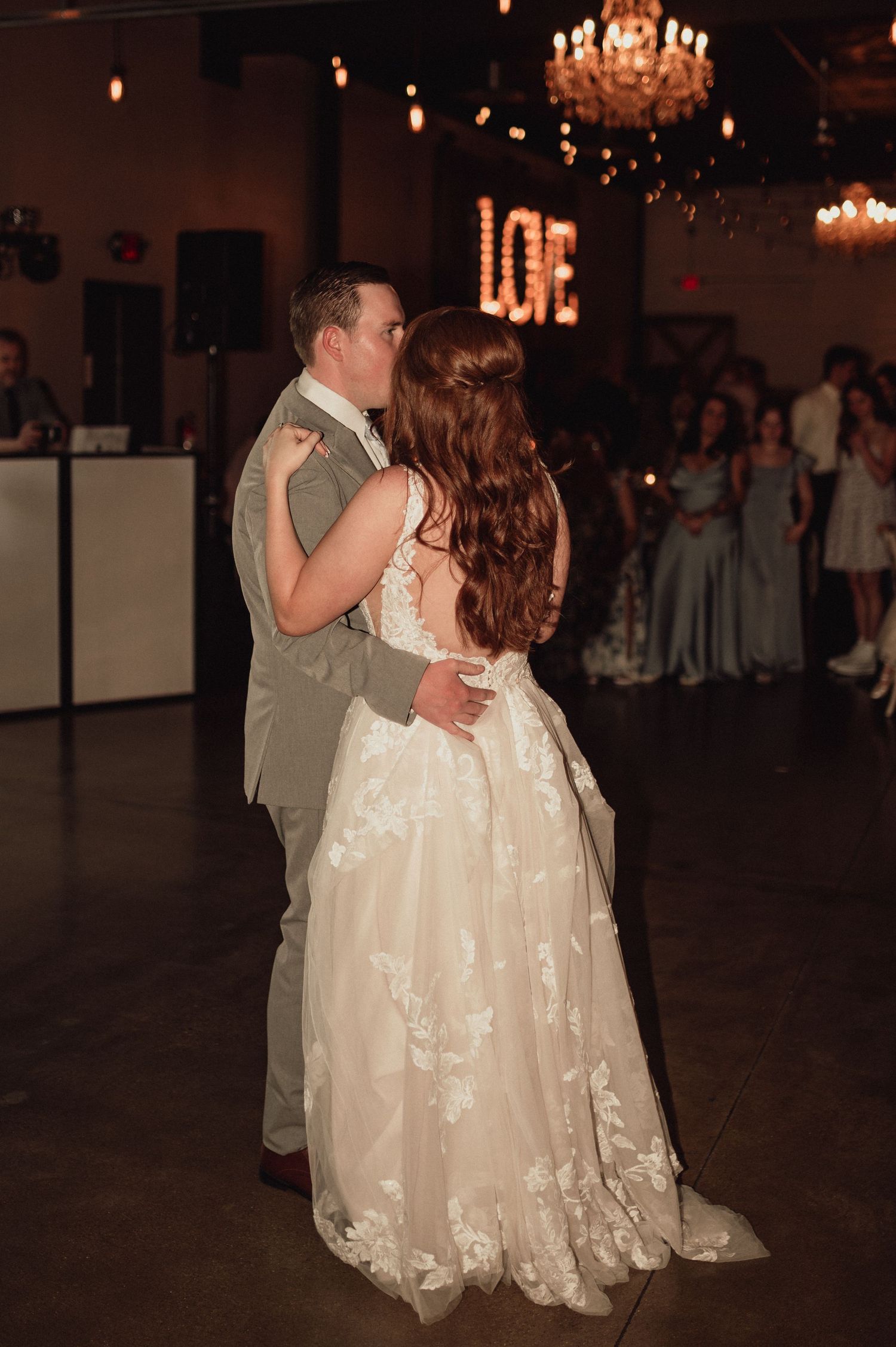 A couple shares their first dance at a wedding reception under elegant crystal chandeliers in a dimly lit ballroom.