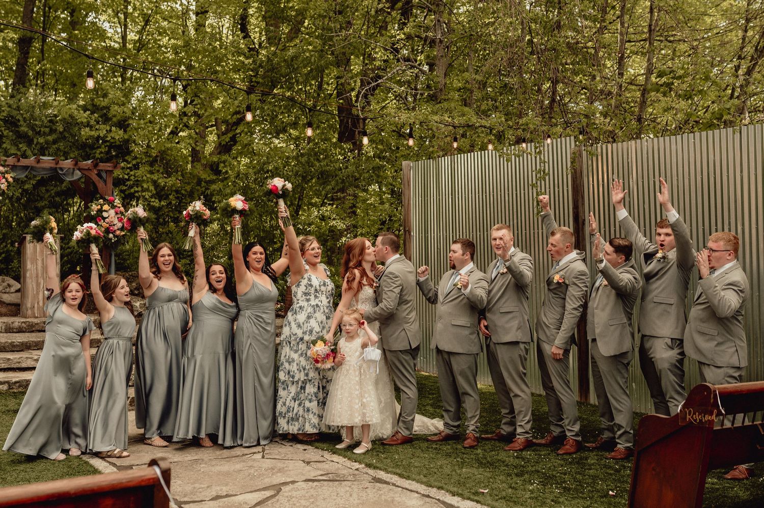 Wedding party in gray and pink attire poses together for group photos in an outdoor garden setting.