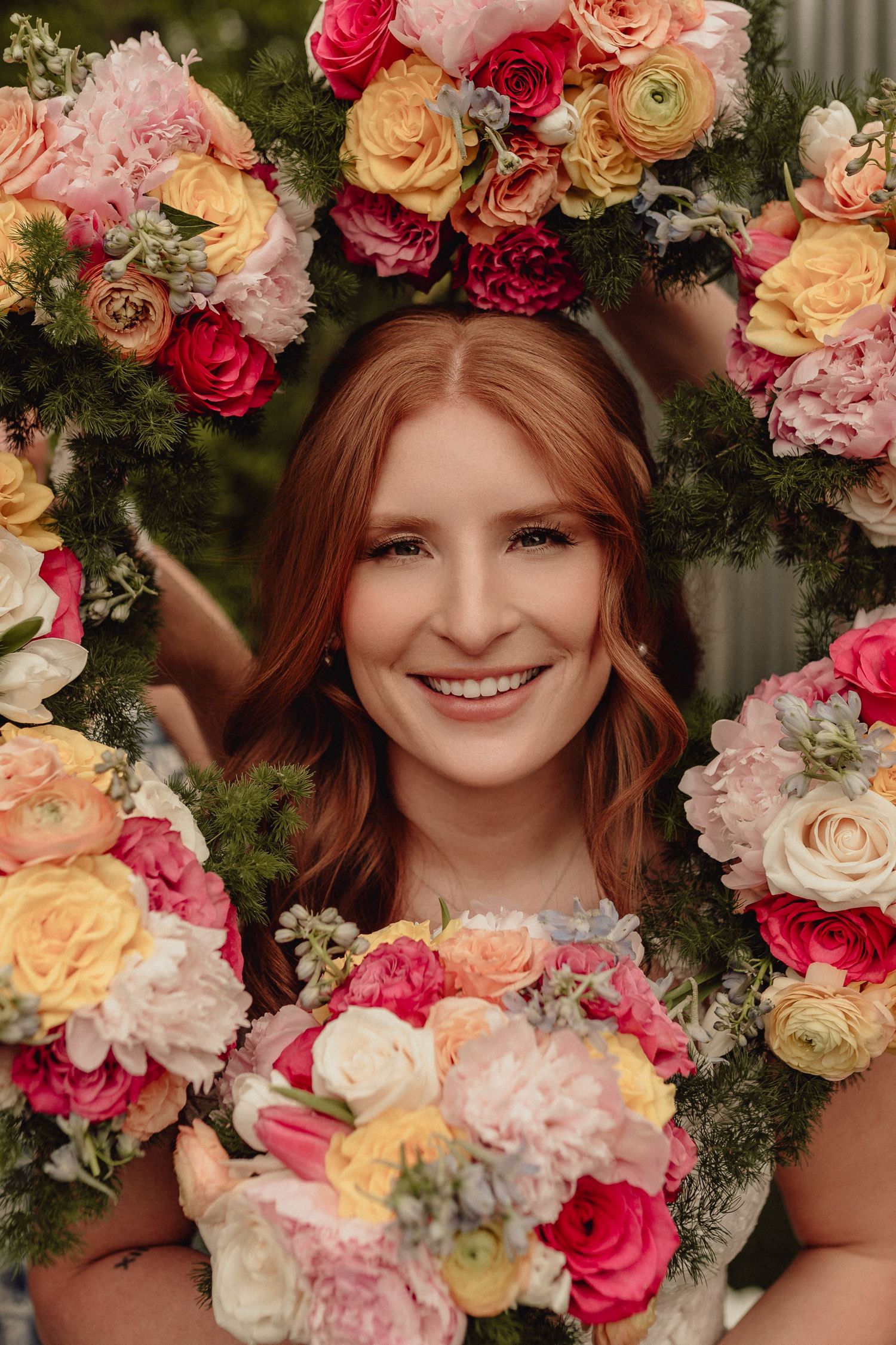 Beautiful floral portrait featuring a crown of pink, peach and cream roses with lush greenery in a romantic garden setting.