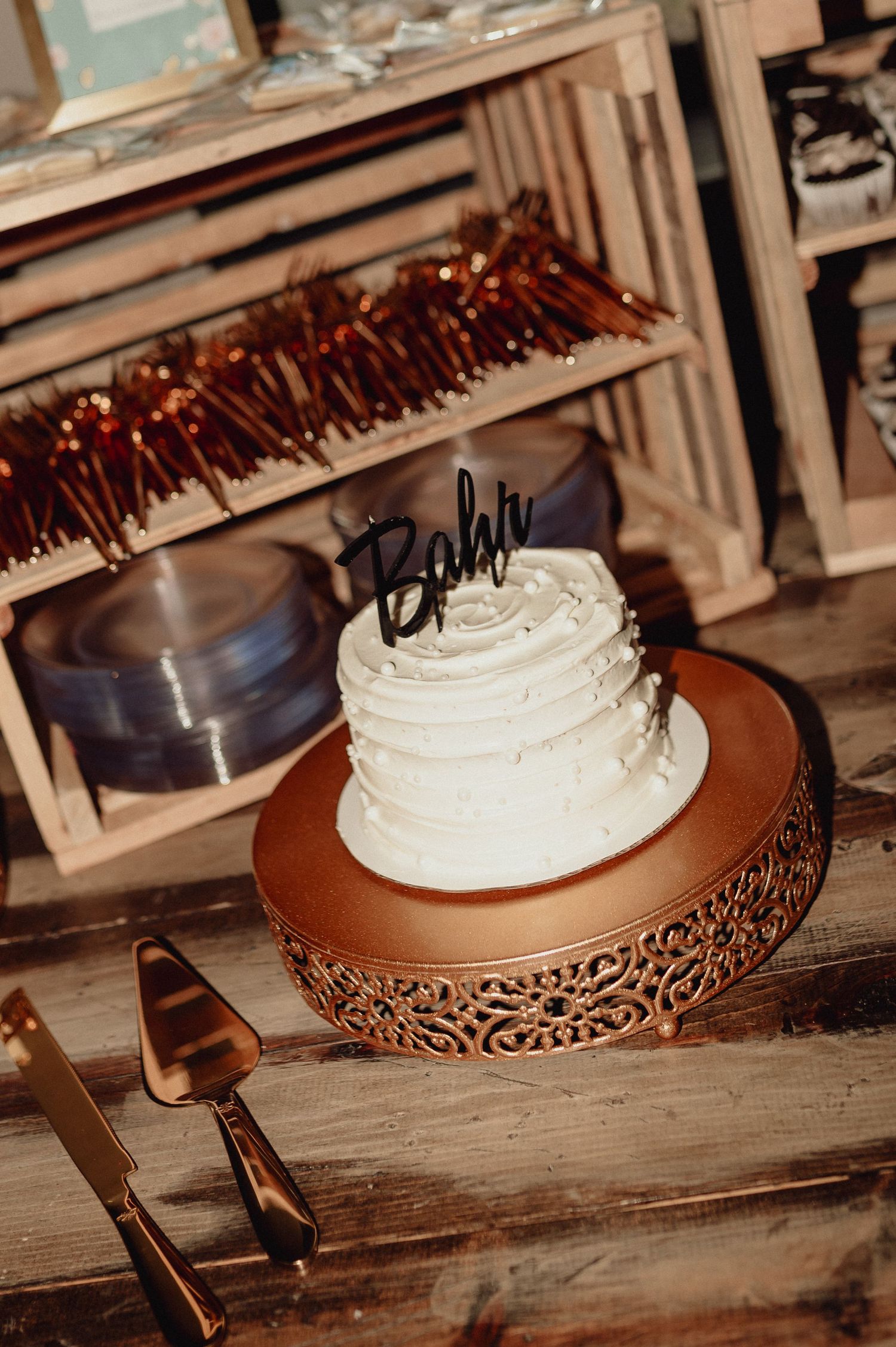 White frosted cake displayed on an ornate copper-colored cake stand against rustic wooden surface in vintage setting.