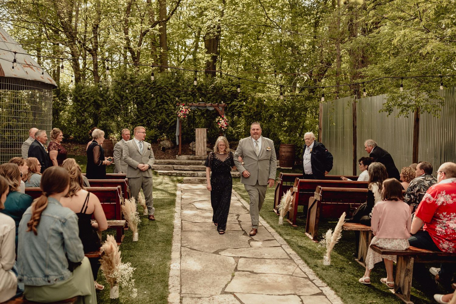 Wedding guests gather on wooden benches in a serene outdoor garden setting for a ceremony.