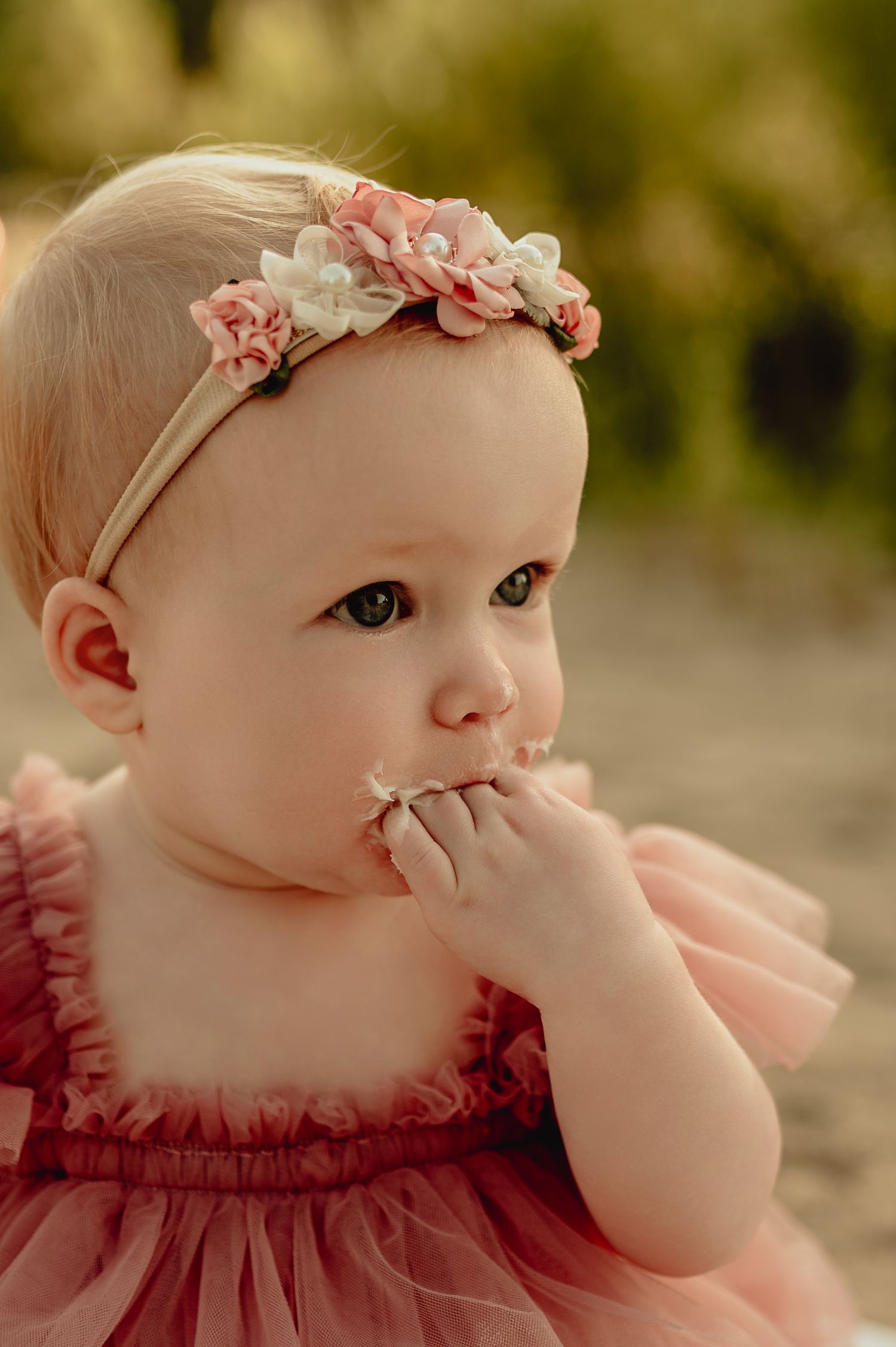 Close-up of baby wearing pink dress and floral headband during cake smash session.